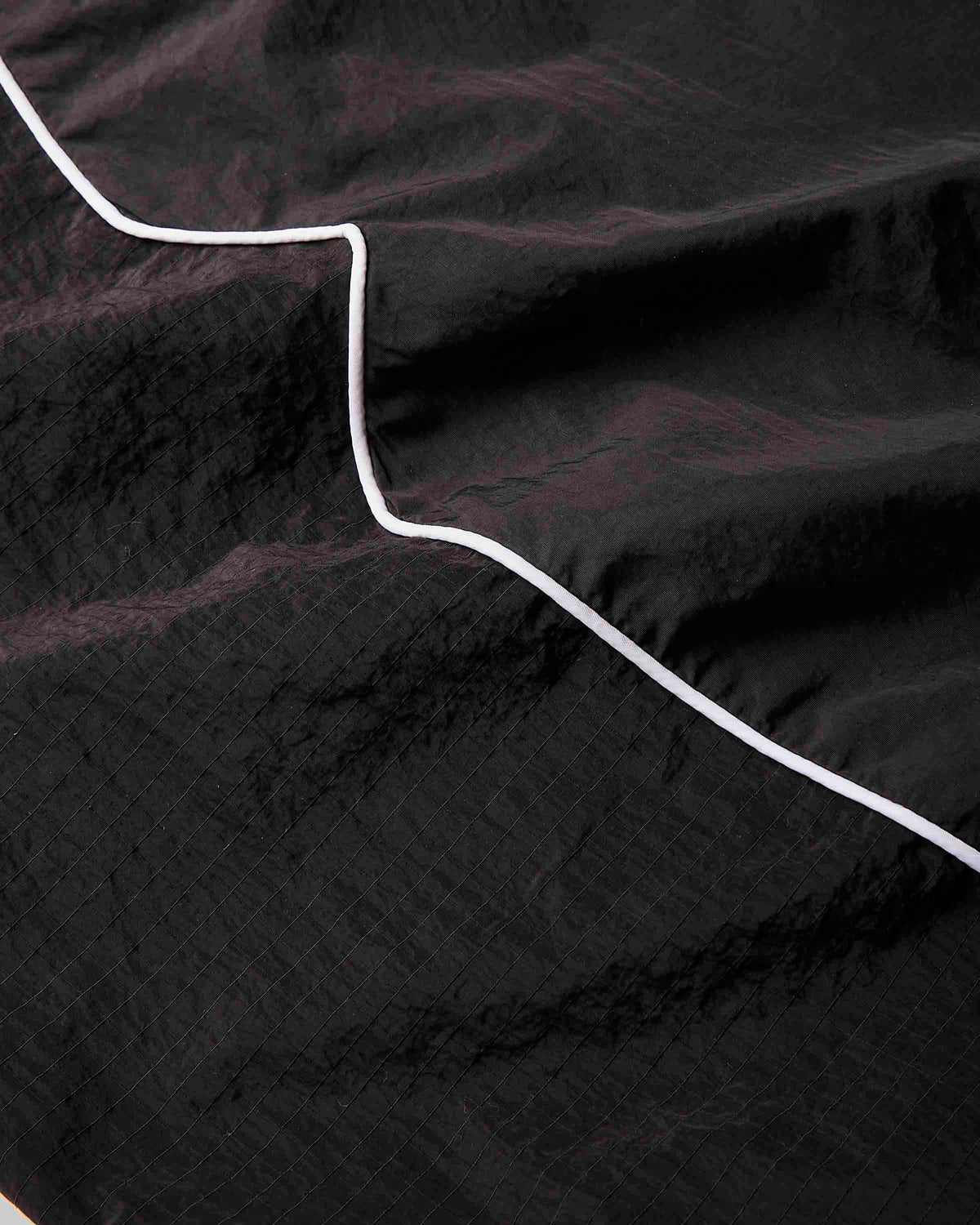 A close-up of a black crinkled fabric with a thin white stitched or printed line running diagonally across it.