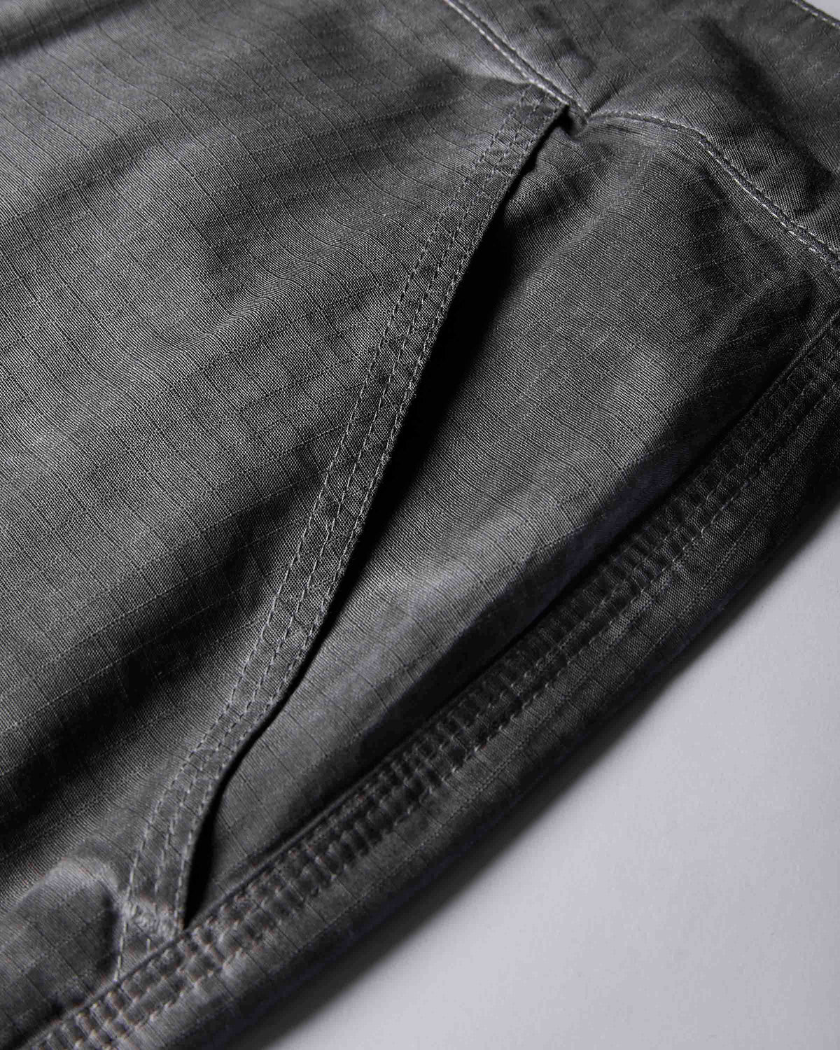 Close-up detail shot of dark gray fabric with visible stitching and texture, showing part of a garment or textile fold on a light gray background.