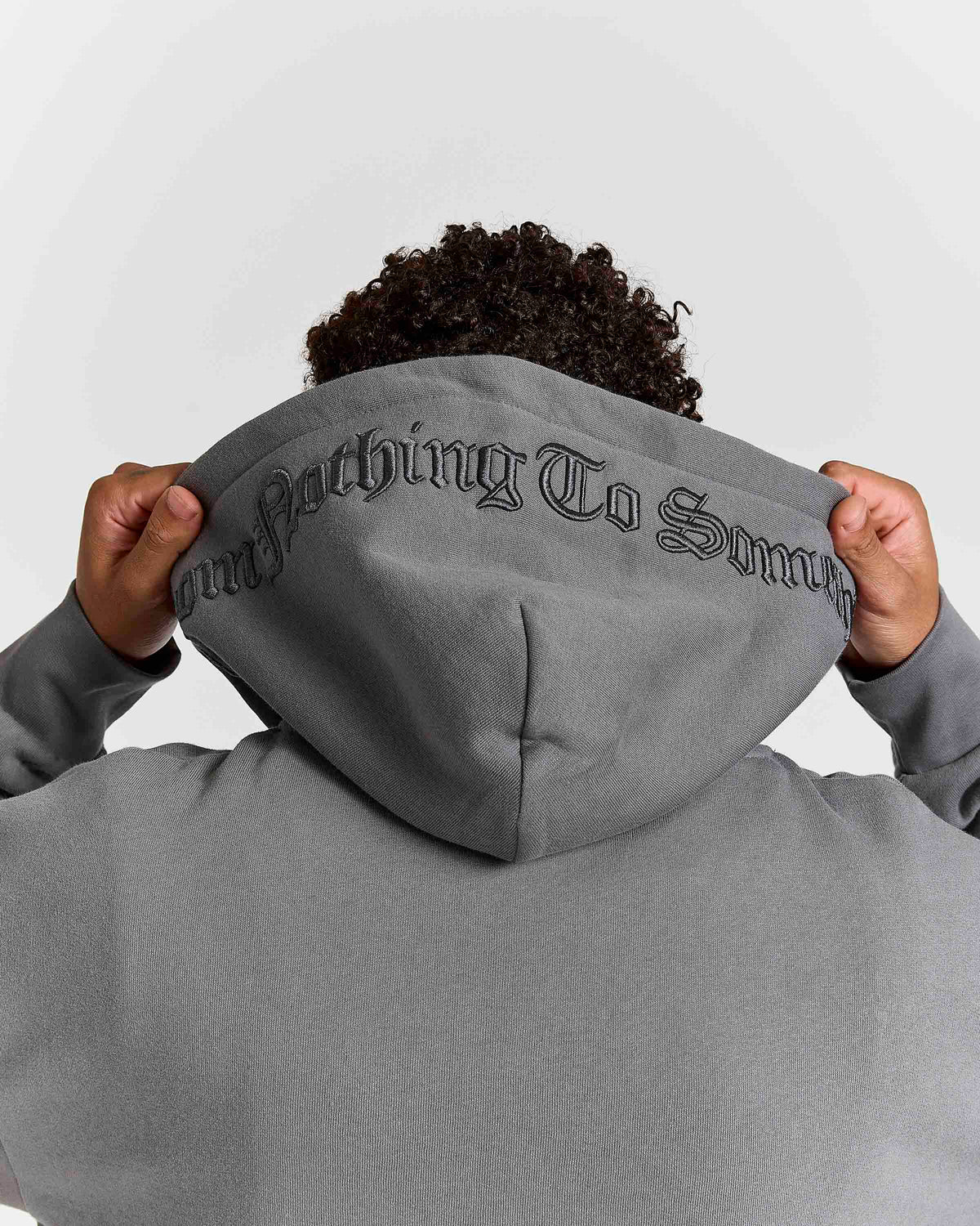 Displays a model wearing the grey lava smoke 'Hoodrich' branded Forza Oversized Zip Through Hoodie featuring the details on the hood