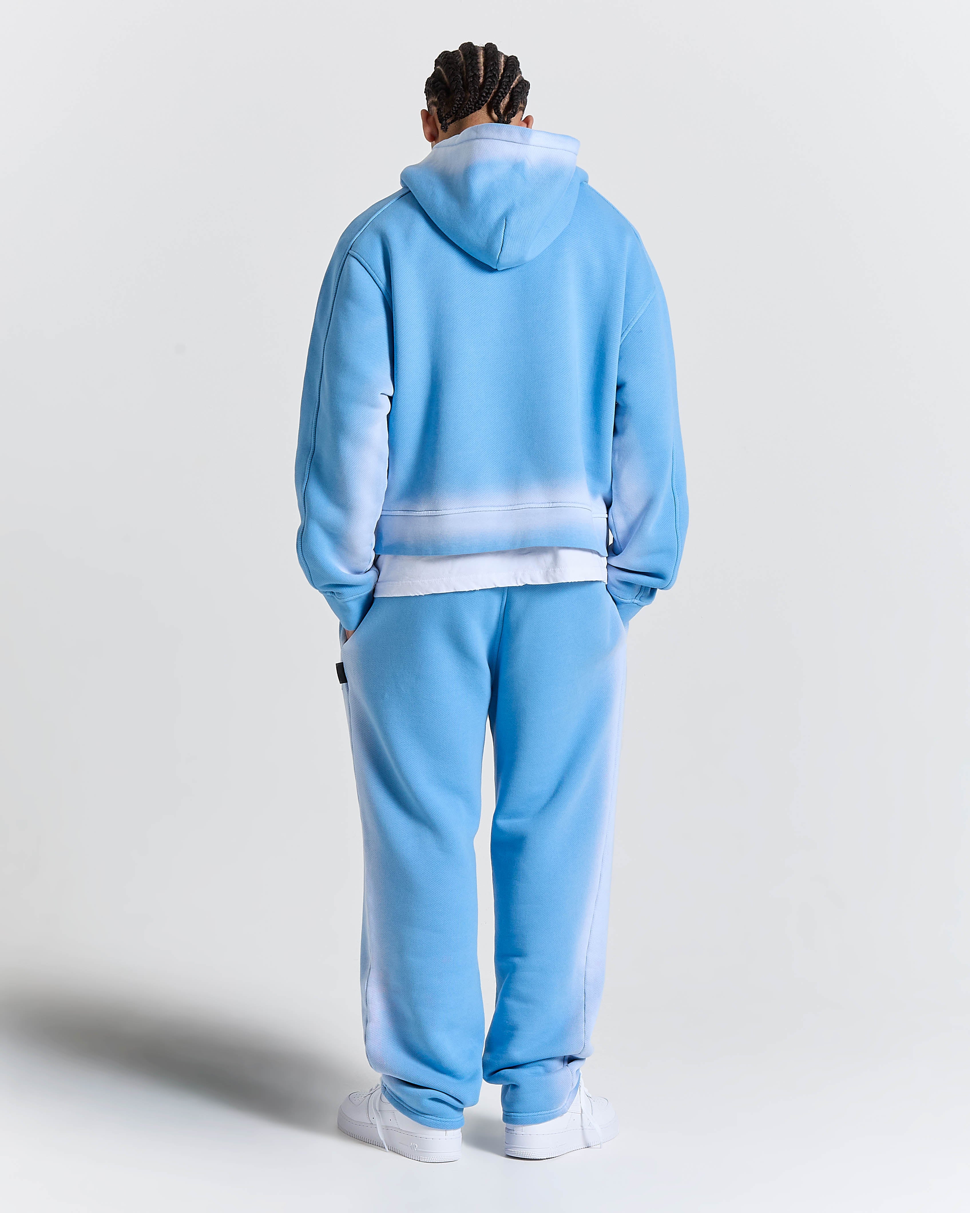Model seen from behind wearing oversized blue joggers, white socks, and white trainers.