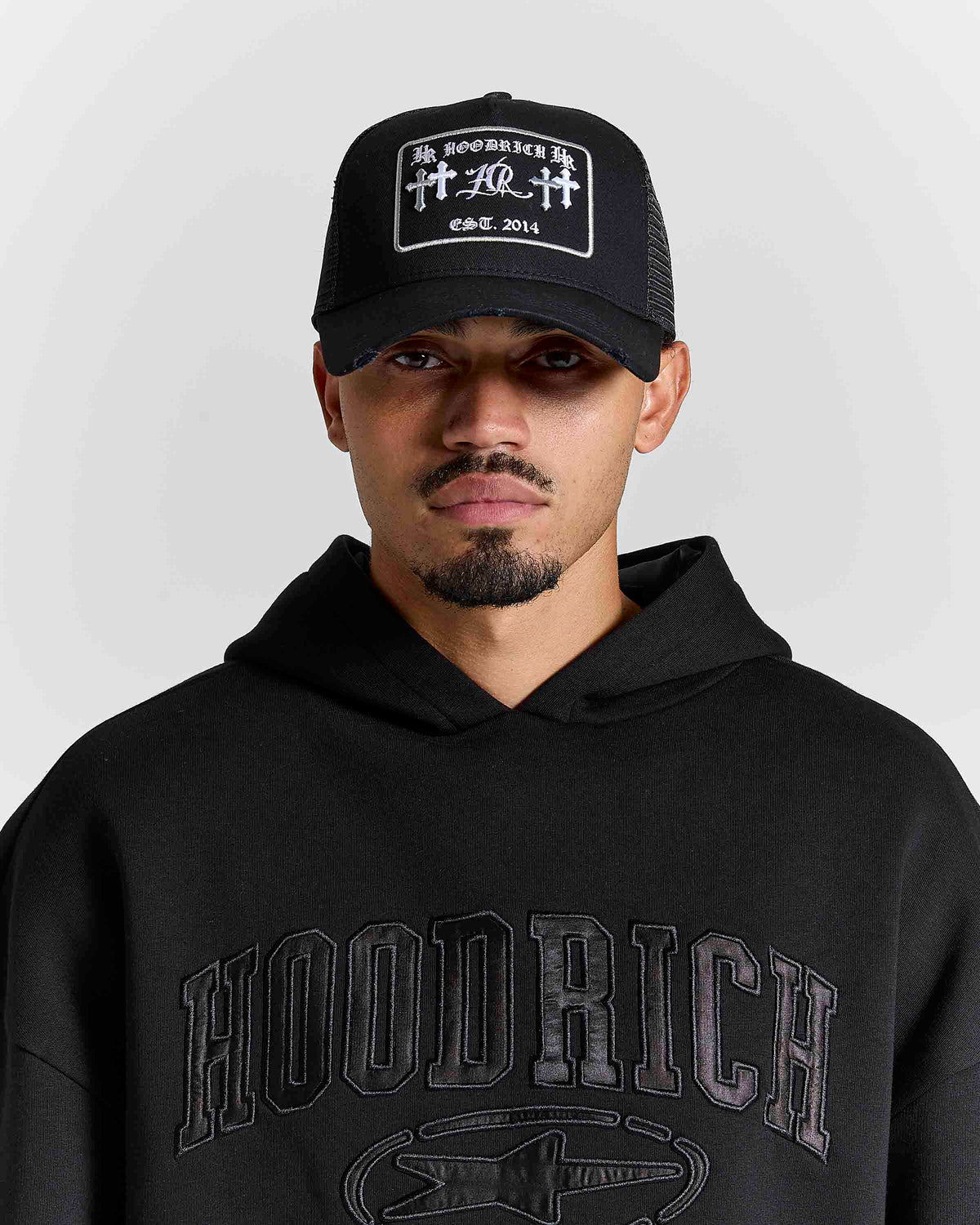 Displays a model wearing the black & grey 'Hoodrich' branded Nocturn Trucker Cap