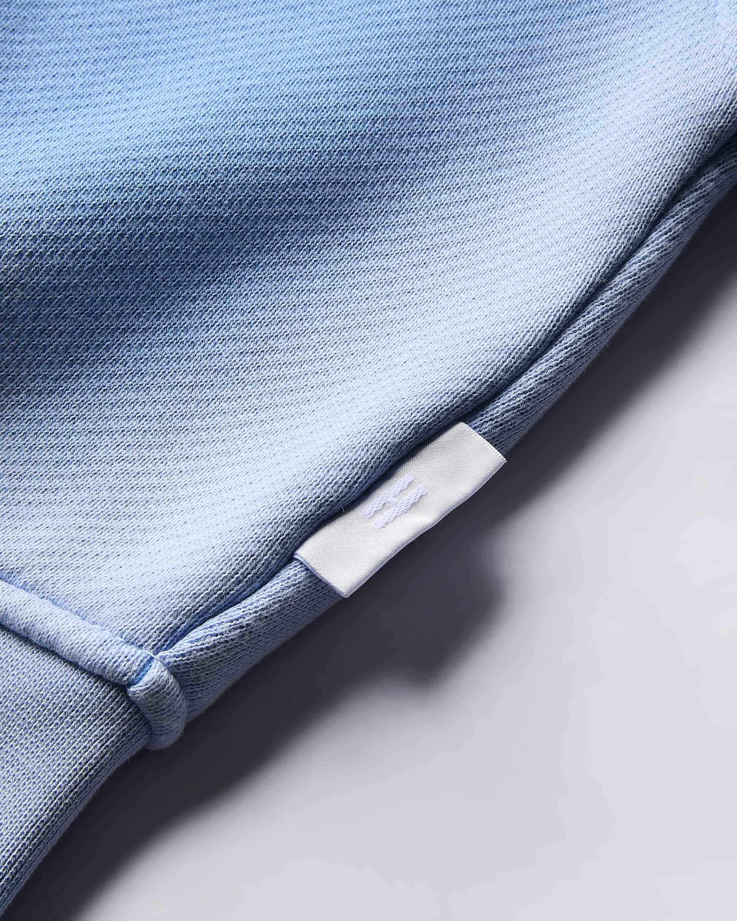Close-up of the small white branded tab on the side of the blue cropped hoodie.