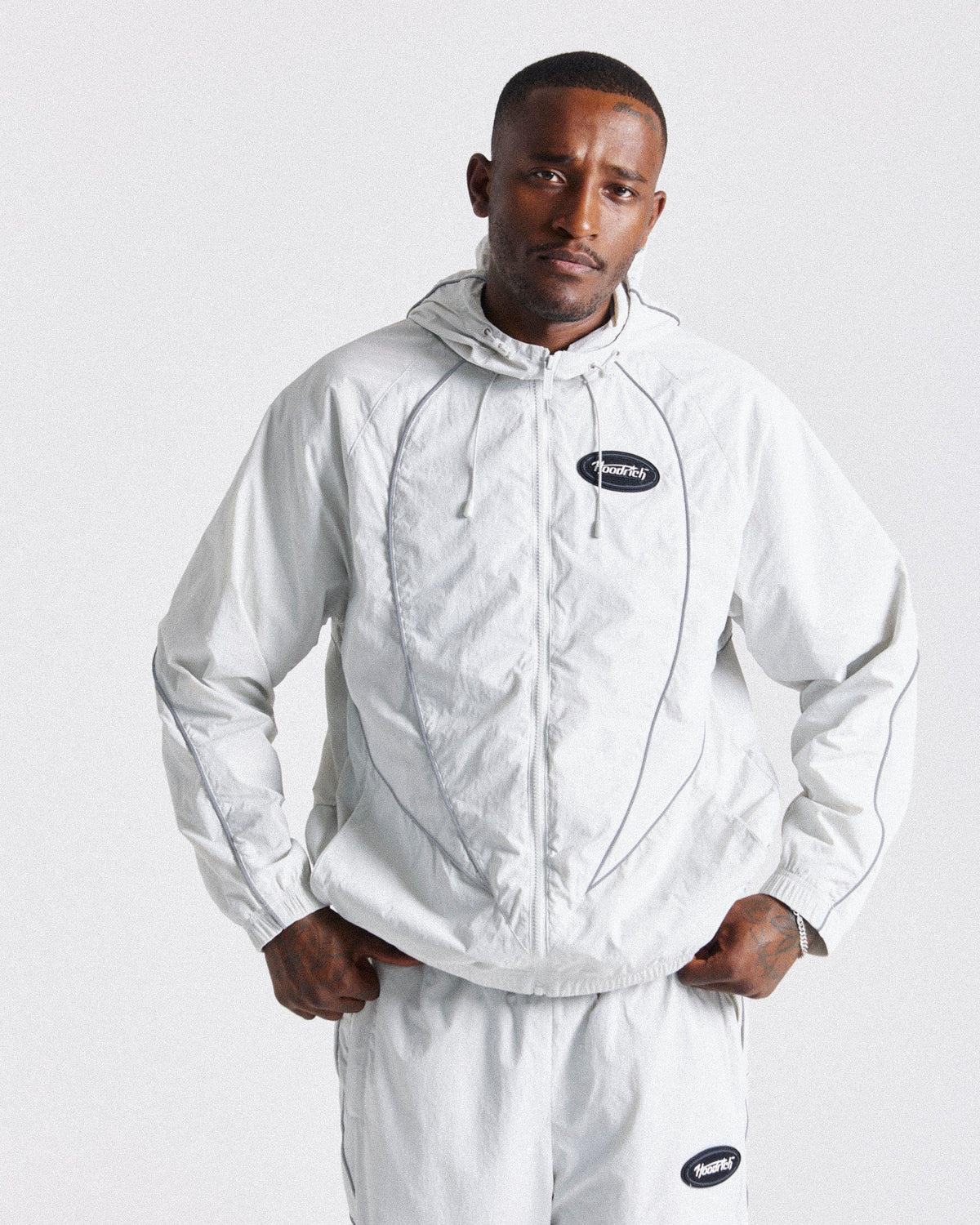Displays a model wearing the Grey 'Hoodrich' branded men's Cypher Woven Full Tracksuit