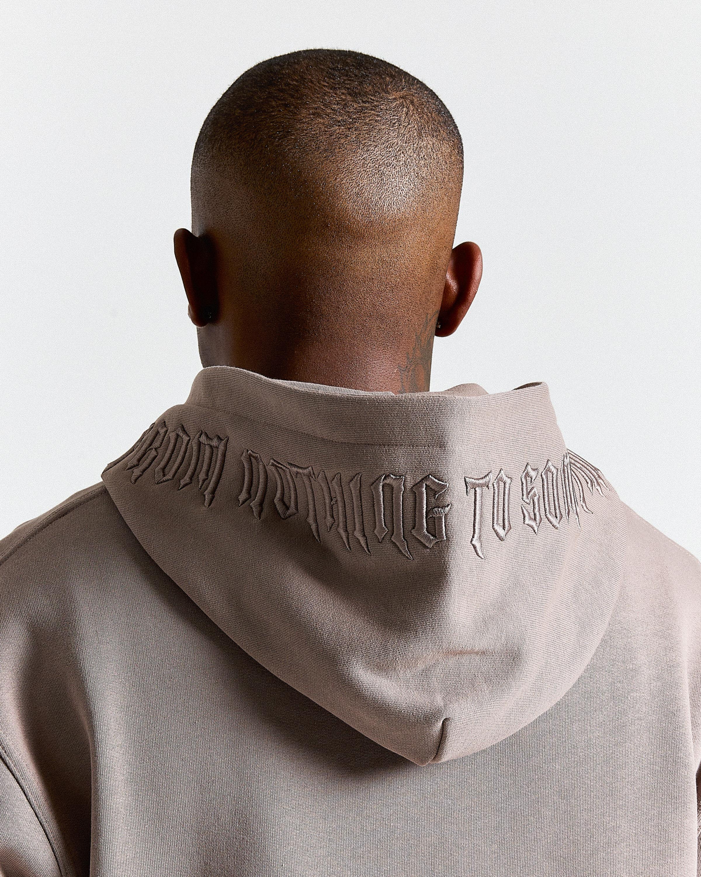 Person wearing a beige hoodie with text on the back against a light gray background
