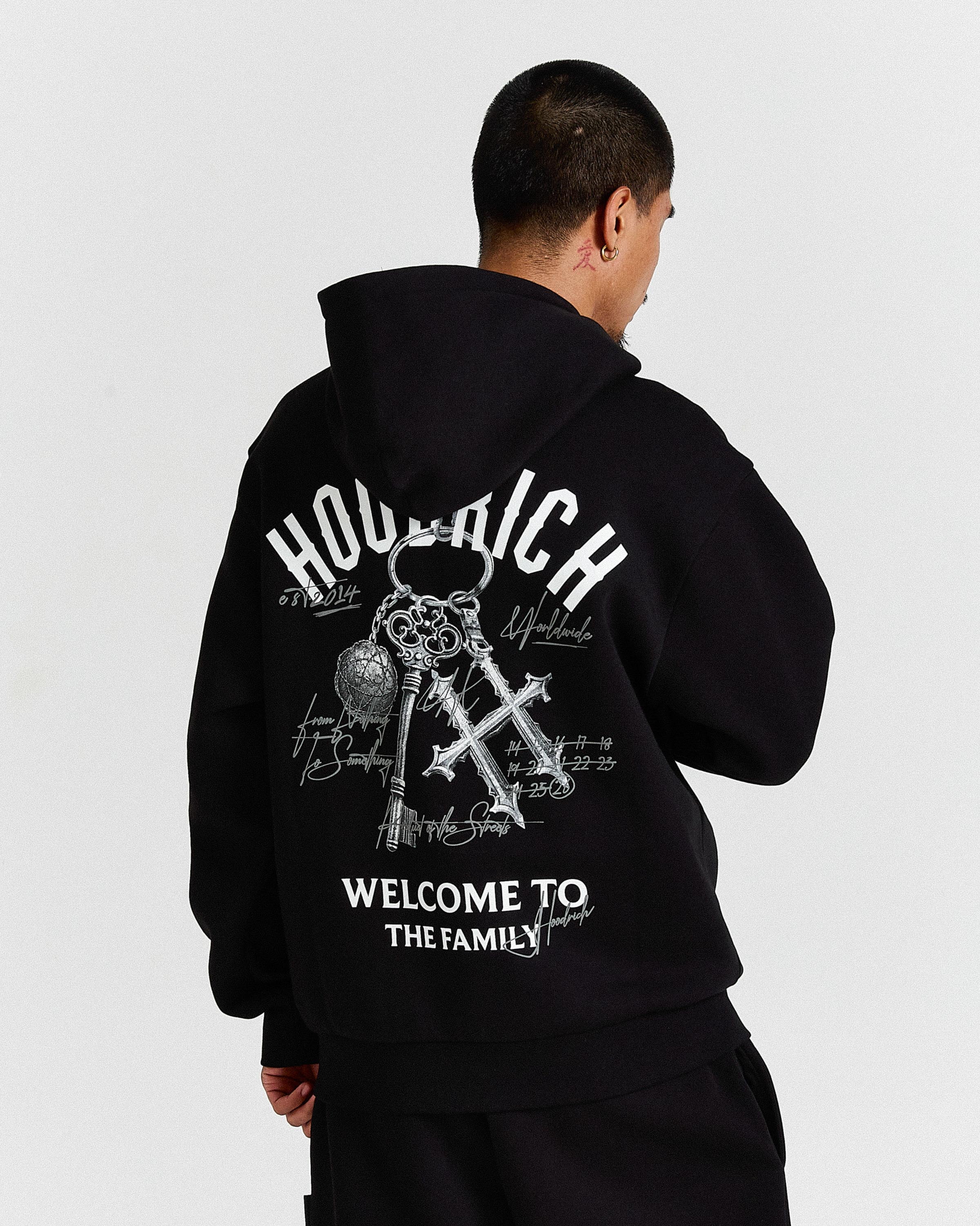 Person wearing a black hoodie with white text and graphics on the back, standing against a light gray background.