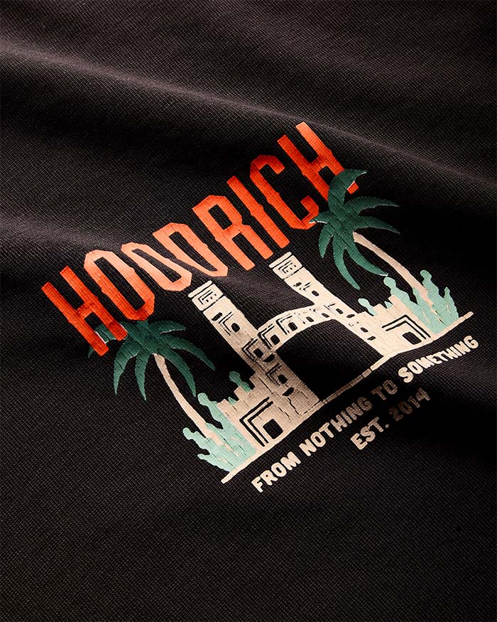 Close-up of a black t-shirt featuring a colorful graphic print with the word 'HOORICH' in orange, green palm trees, a white building illustration, and the text 'FROM NOTHING TO SOMETHING EST. 2014'.