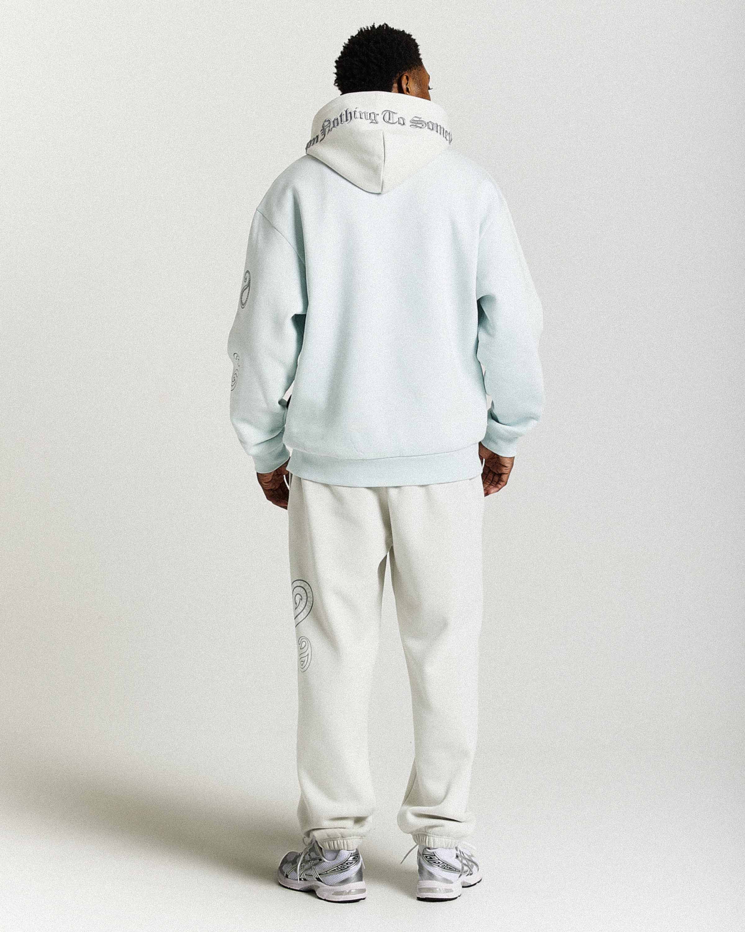 Person wearing a light blue hoodie and white pants with brand logos on a white background