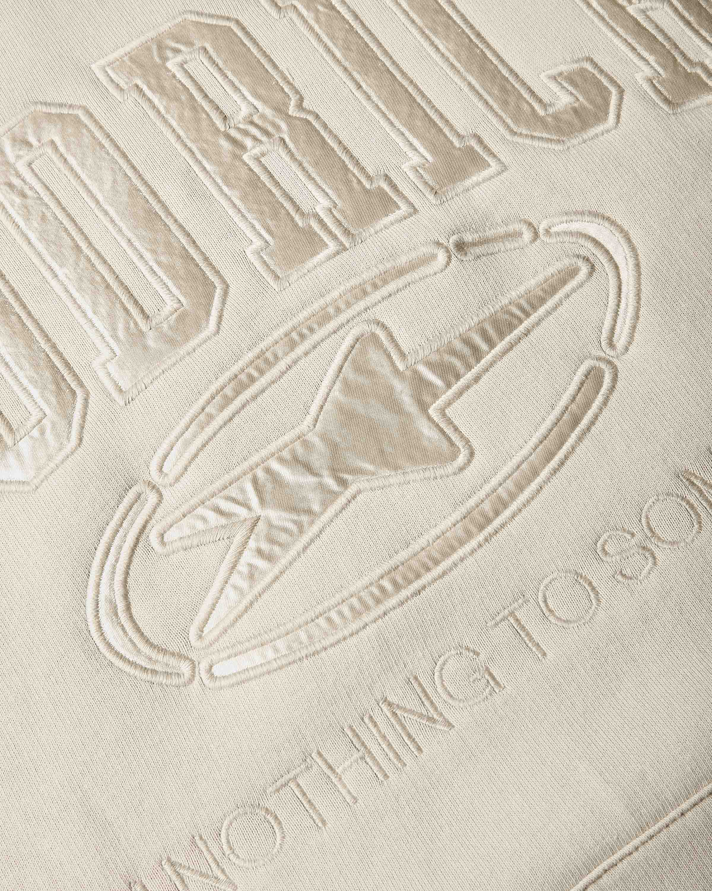 Close-up of a beige embroidered fabric with the Hoodrich branding 