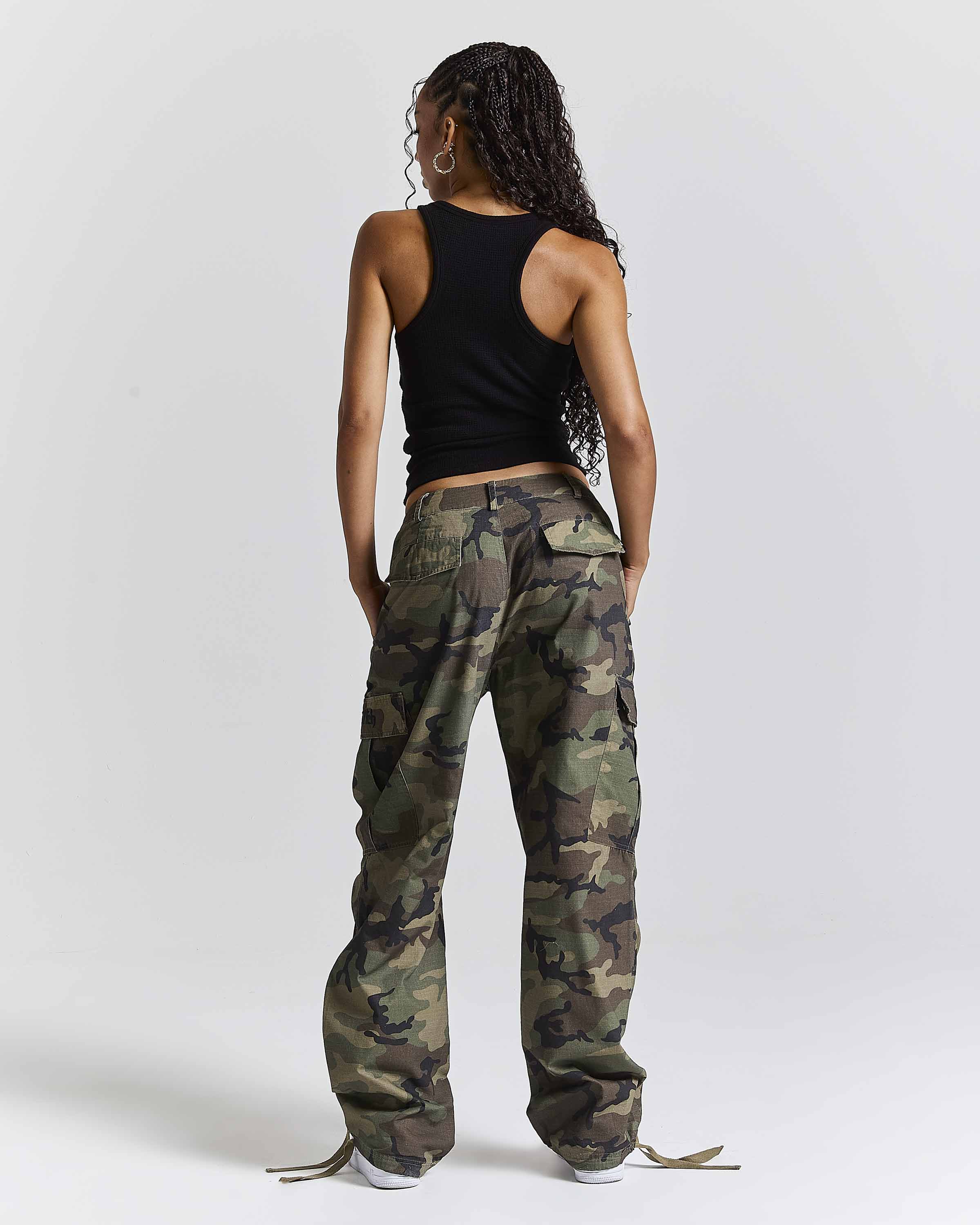 A model shown from the back wearing a black sleeveless top and loose-fit camouflage cargo pants against a light gray studio background.