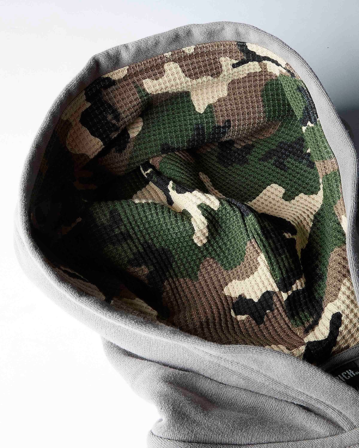 Close-up of a gray fleece hood or balaclava-style head covering with a green, brown, black, and beige camouflage waffle-textured lining visible inside.