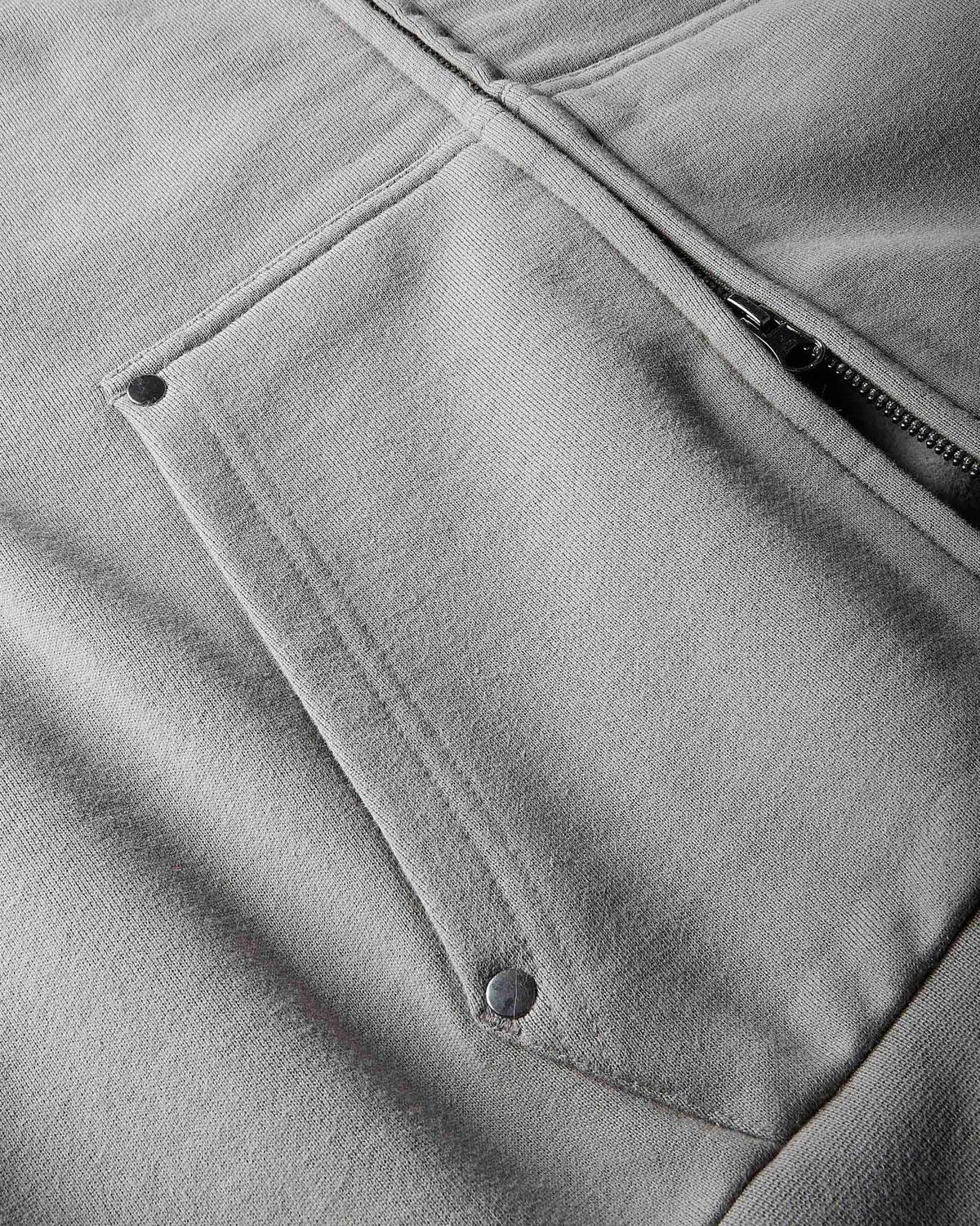 Close-up of a light gray zip-up hoodie showing a pocket with metal snap buttons and a zipper.