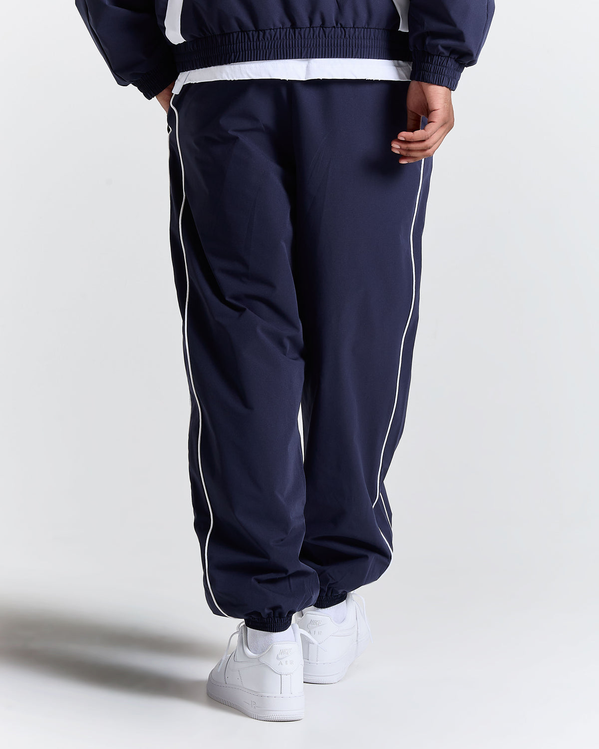 Navy tracksuit with white stripes worn by a person on a light gray background