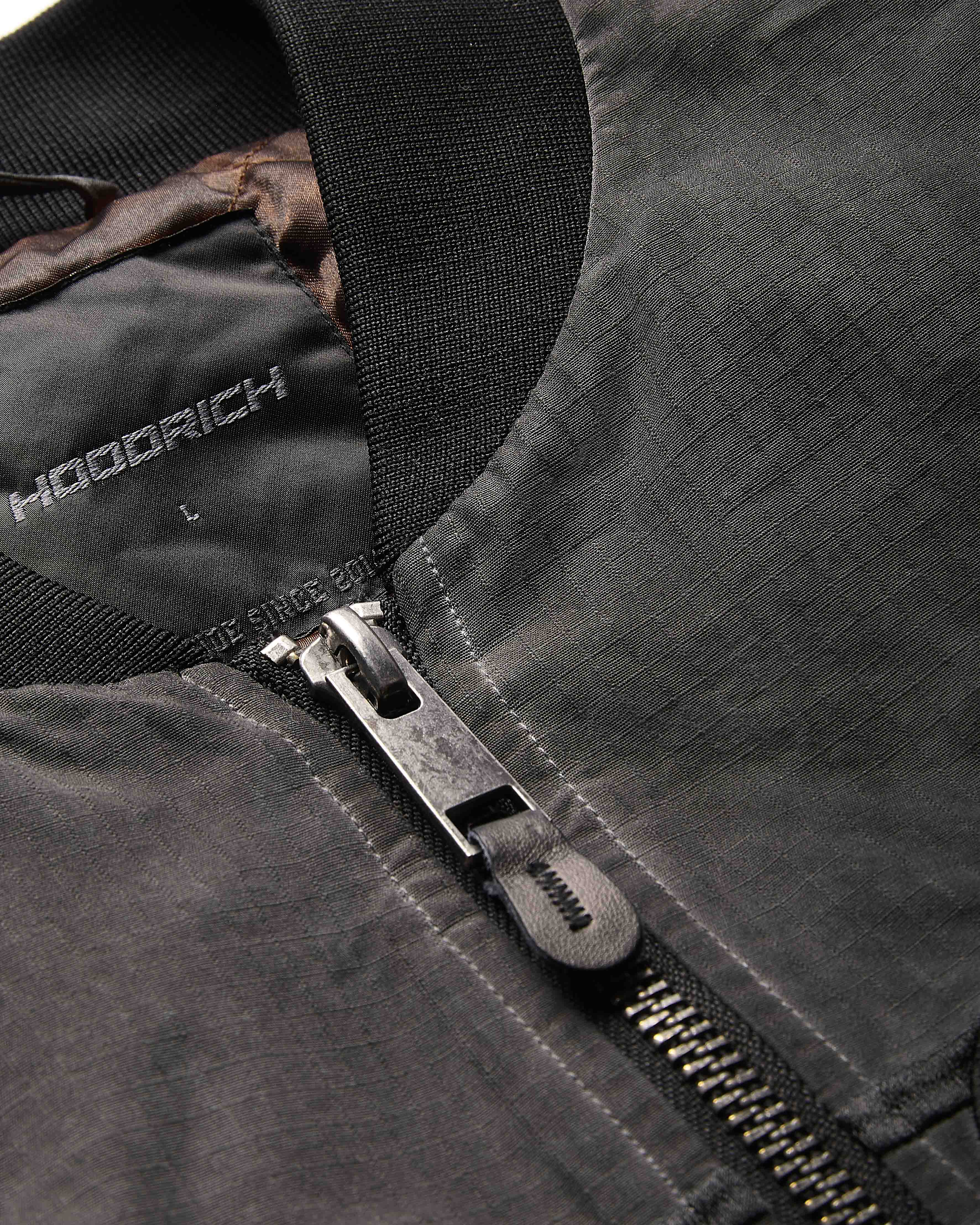 Close-up of a black jacket with a zipper, featuring the brand 'Hoodrich'.
