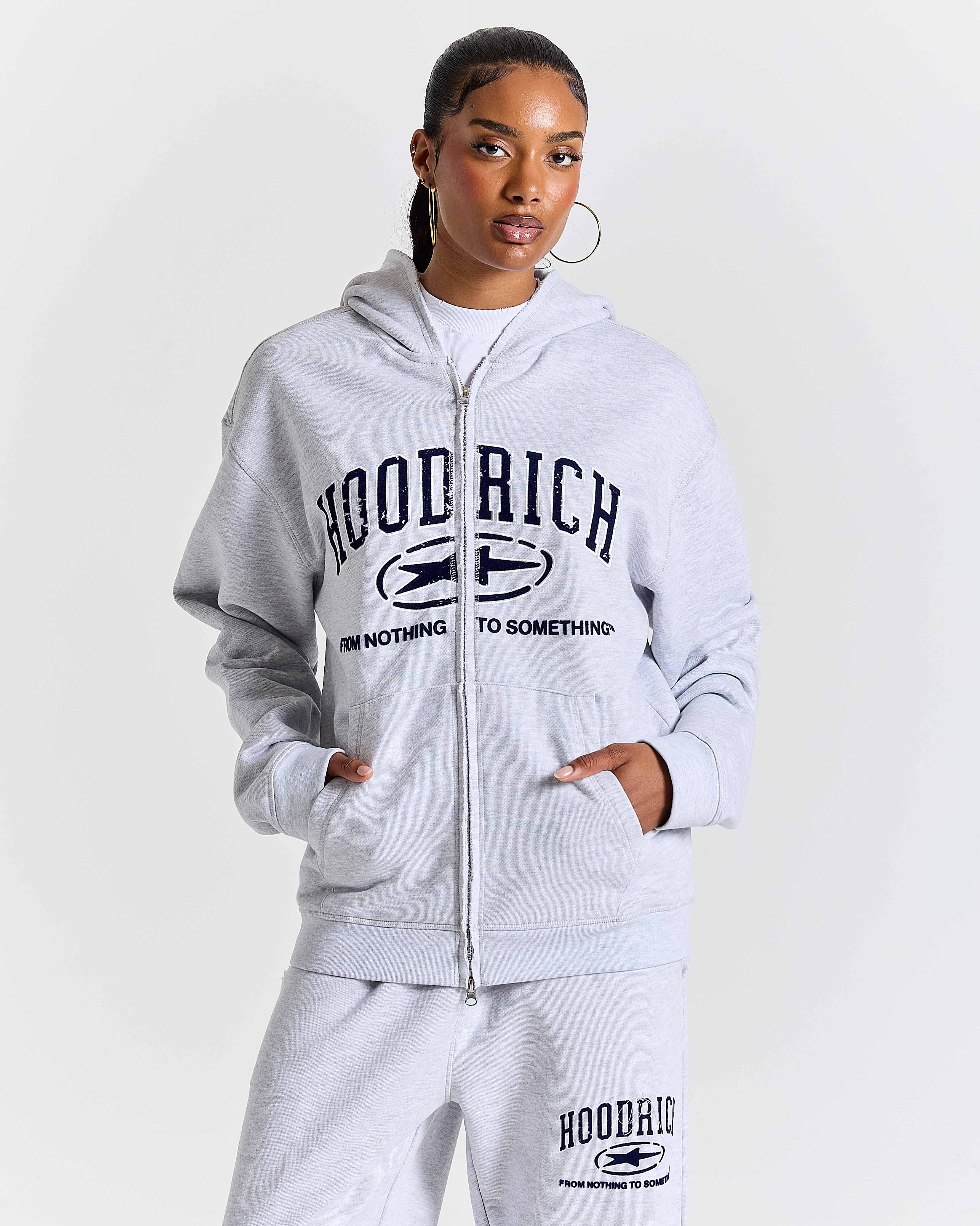 Person wearing a gray 'Hood Rich' tracksuit on a white background