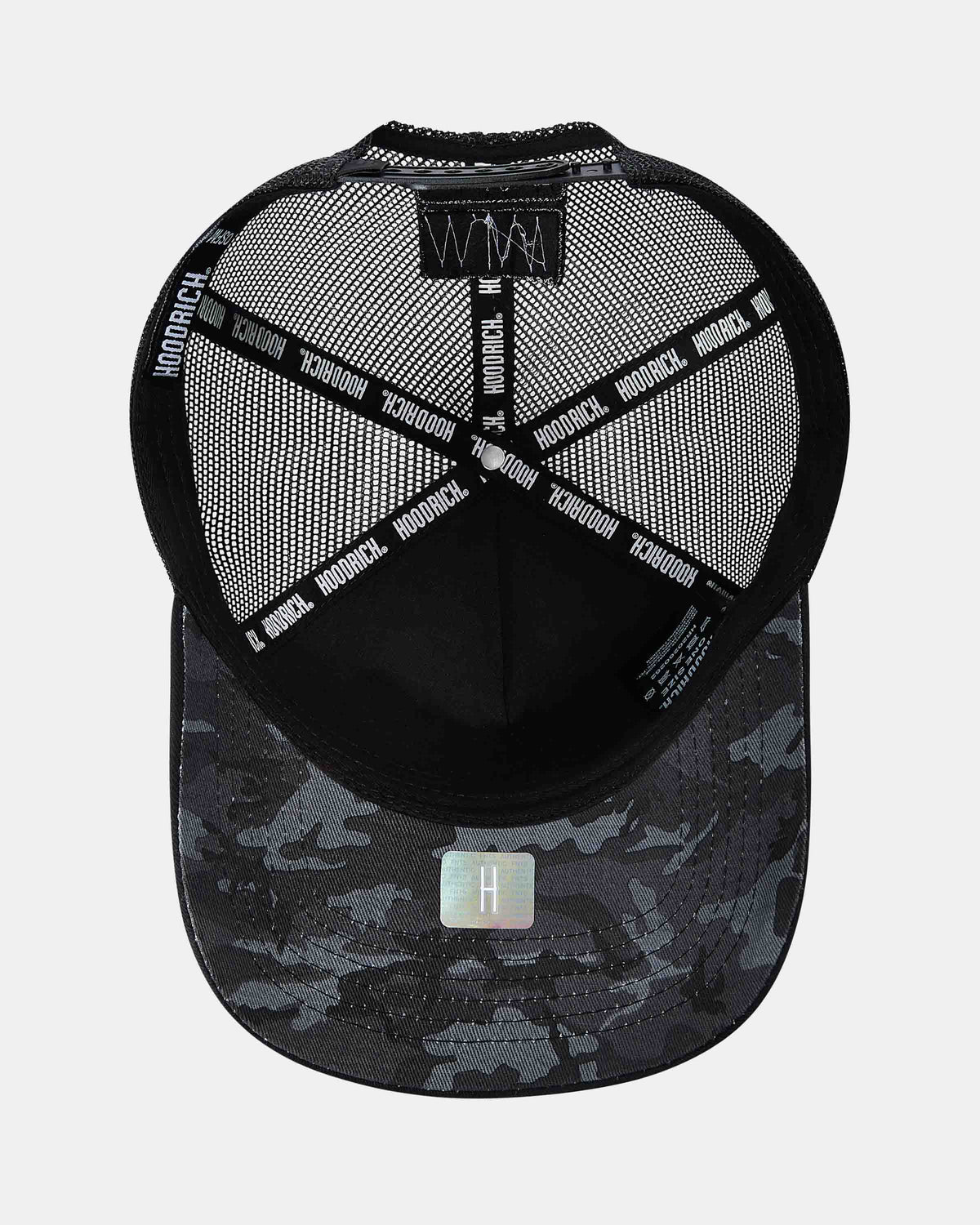 A black and gray camouflage trucker cap shown from the back, featuring a black mesh back with 'HOODRICH' printed repeatedly on the straps, a black embroidered front panel, and a silver holographic 'H' patch on the brim.