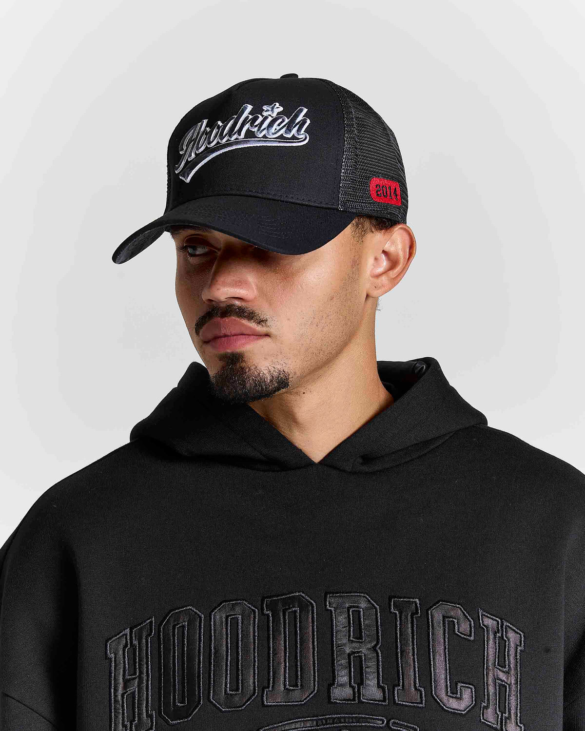 Displays a model wearing the black 'hoodrich' branded Stade 5 Panel Cap