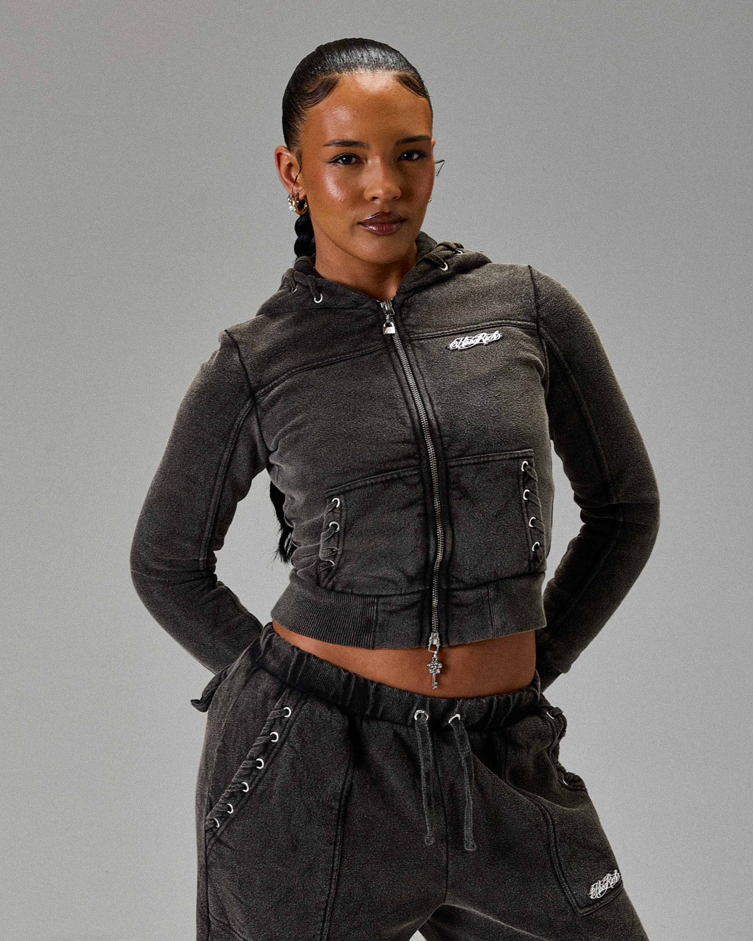 Displays a model wearing the Washed Black 'Hoodrich' branded women's The Winners Circle Token Full Tracksuit