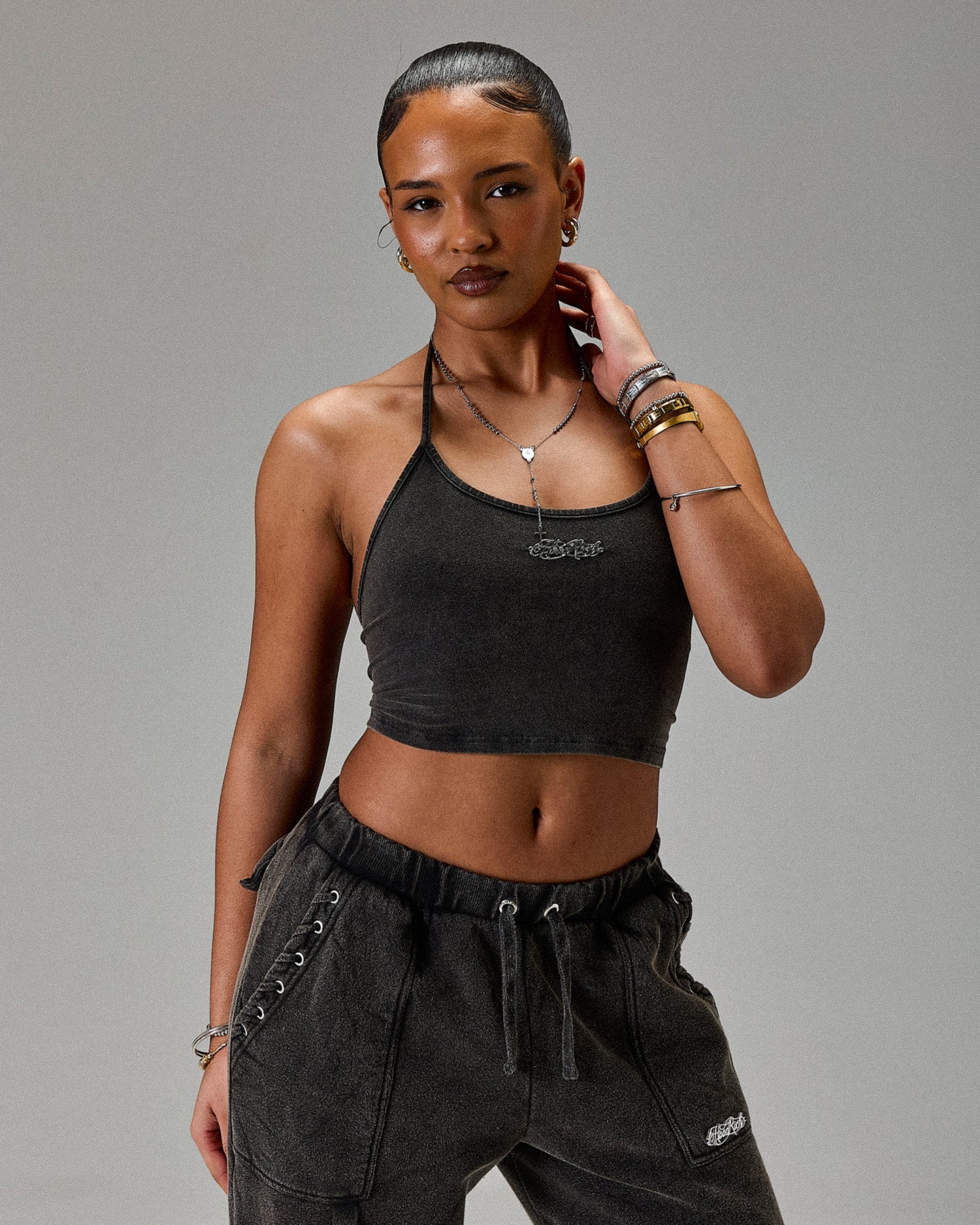 Woman wearing a black crop top and dark pants against a gray background