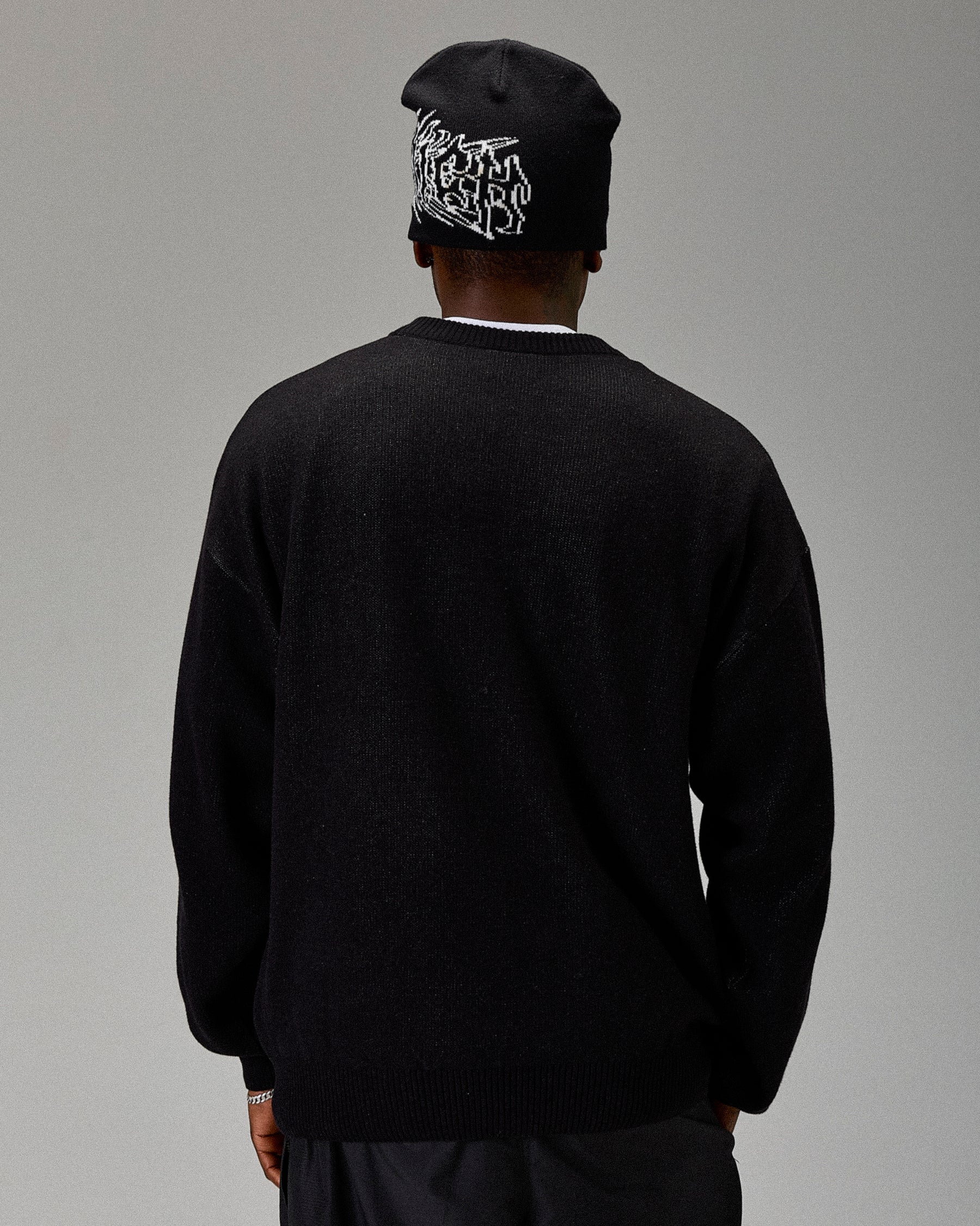 Person wearing a black sweater and beanie with a logo on a gray background