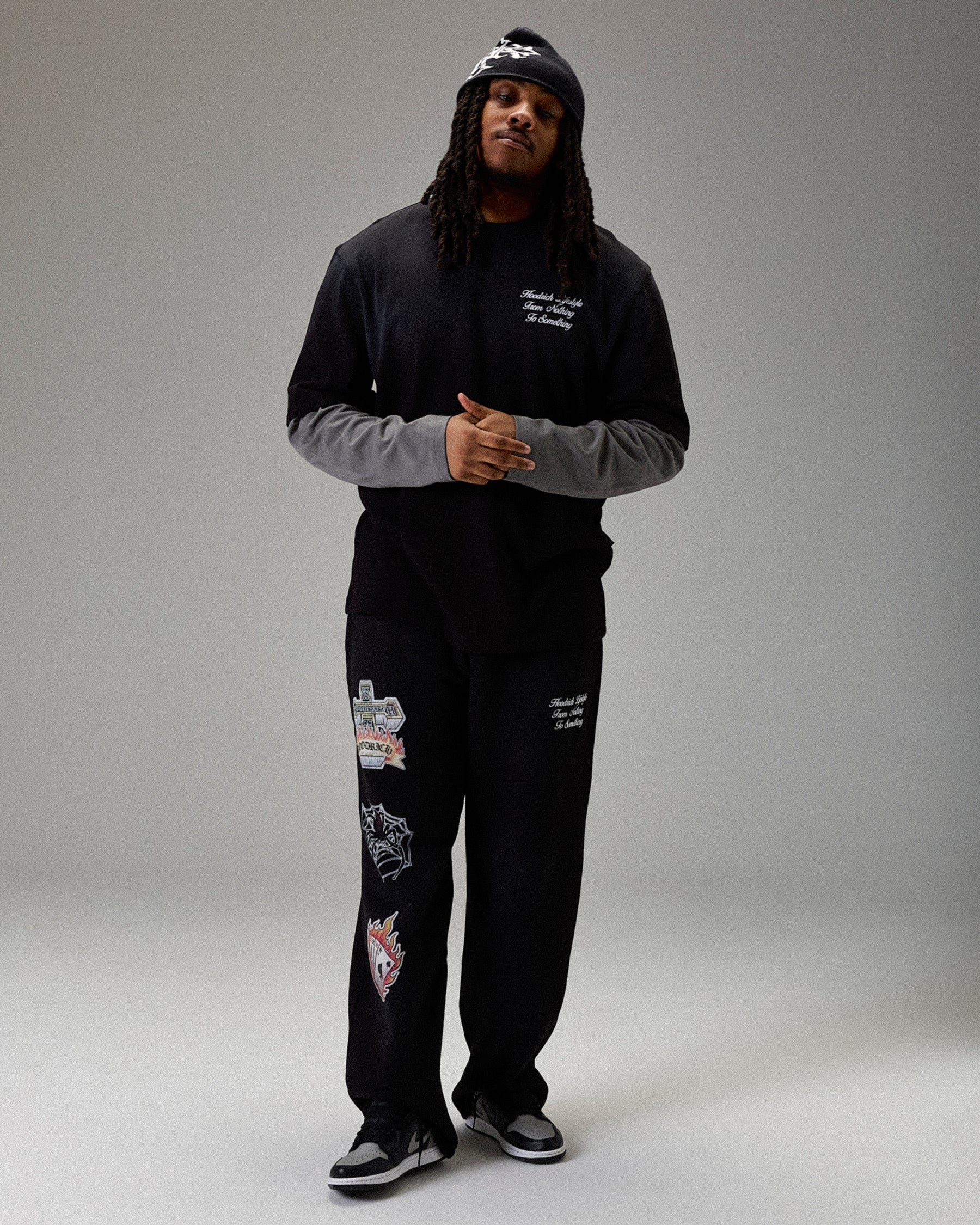 Person wearing a black outfit with patches on a gray background