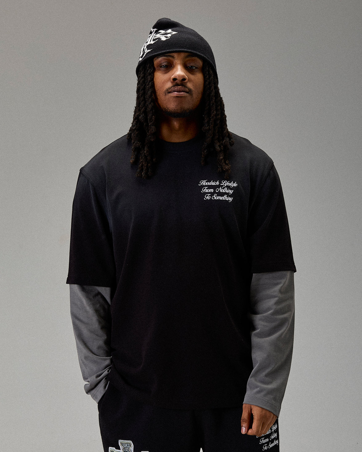 Person wearing a black long-sleeve shirt with text and a black beanie on a gray background