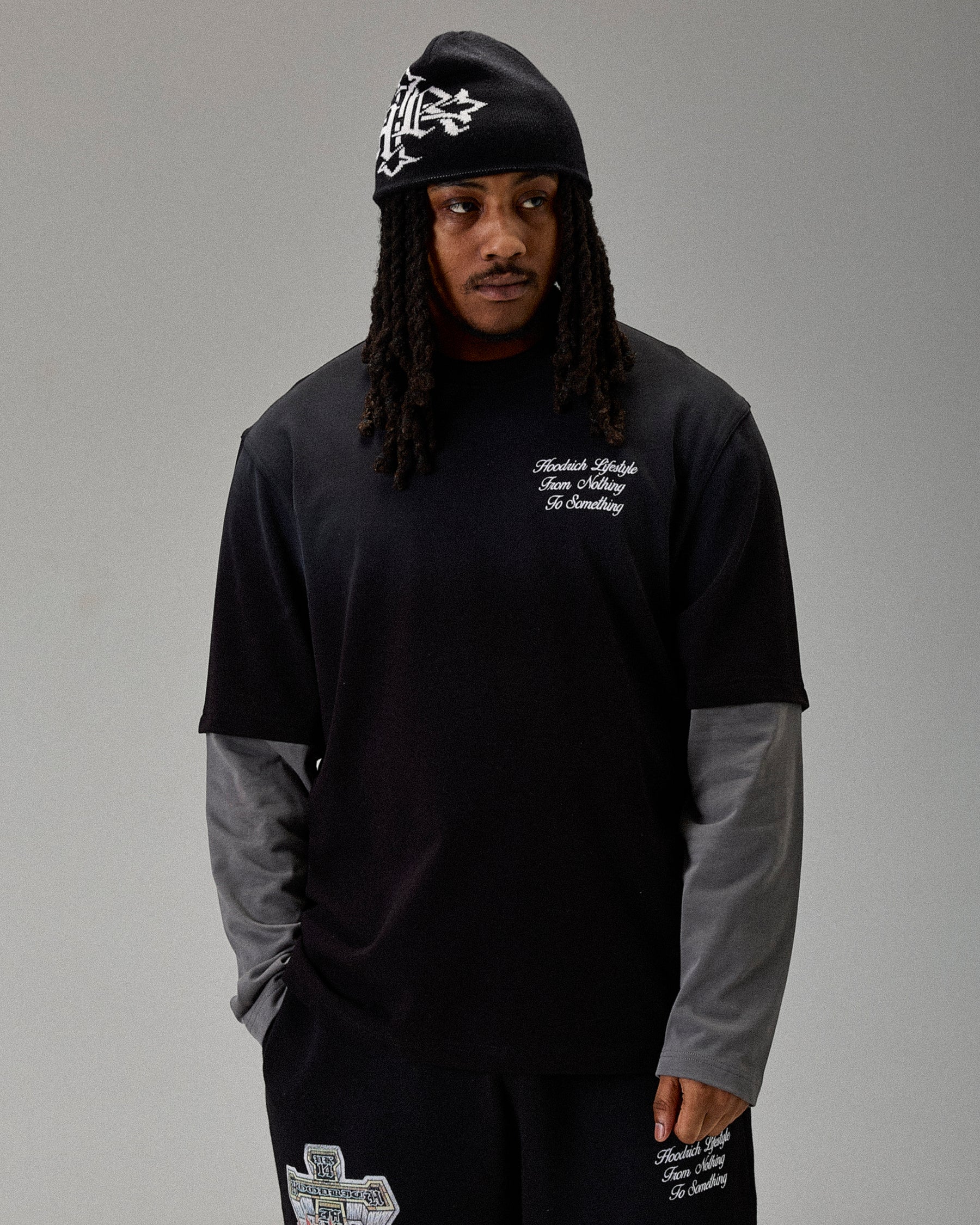 Person wearing a black hoodie and pants with text and graphics on a gray background