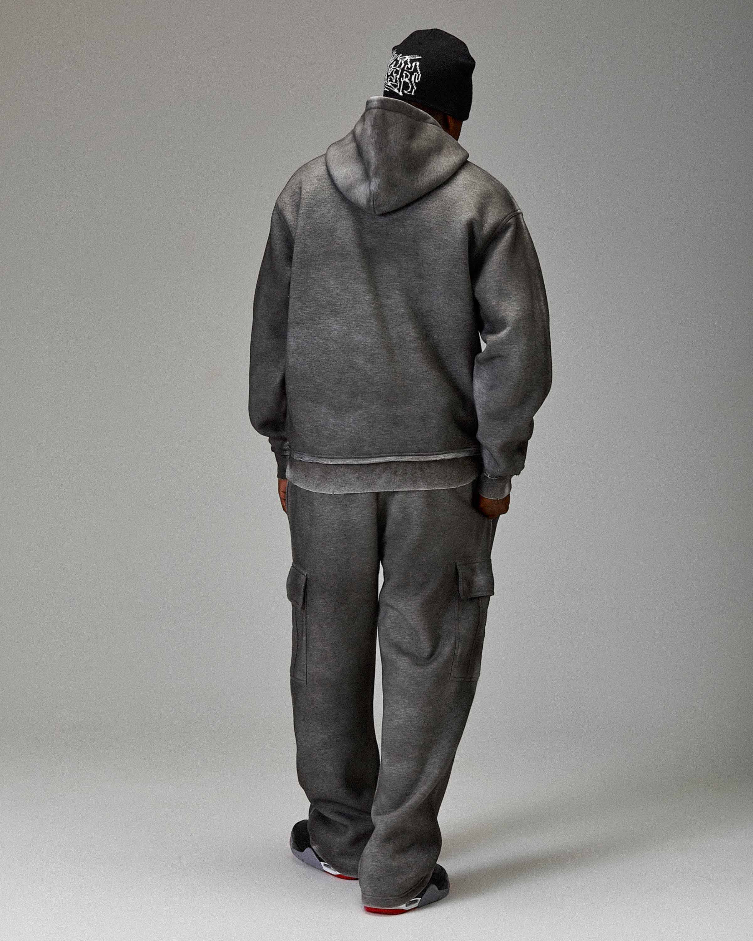 Person wearing a gray tracksuit and black cap on a plain background
