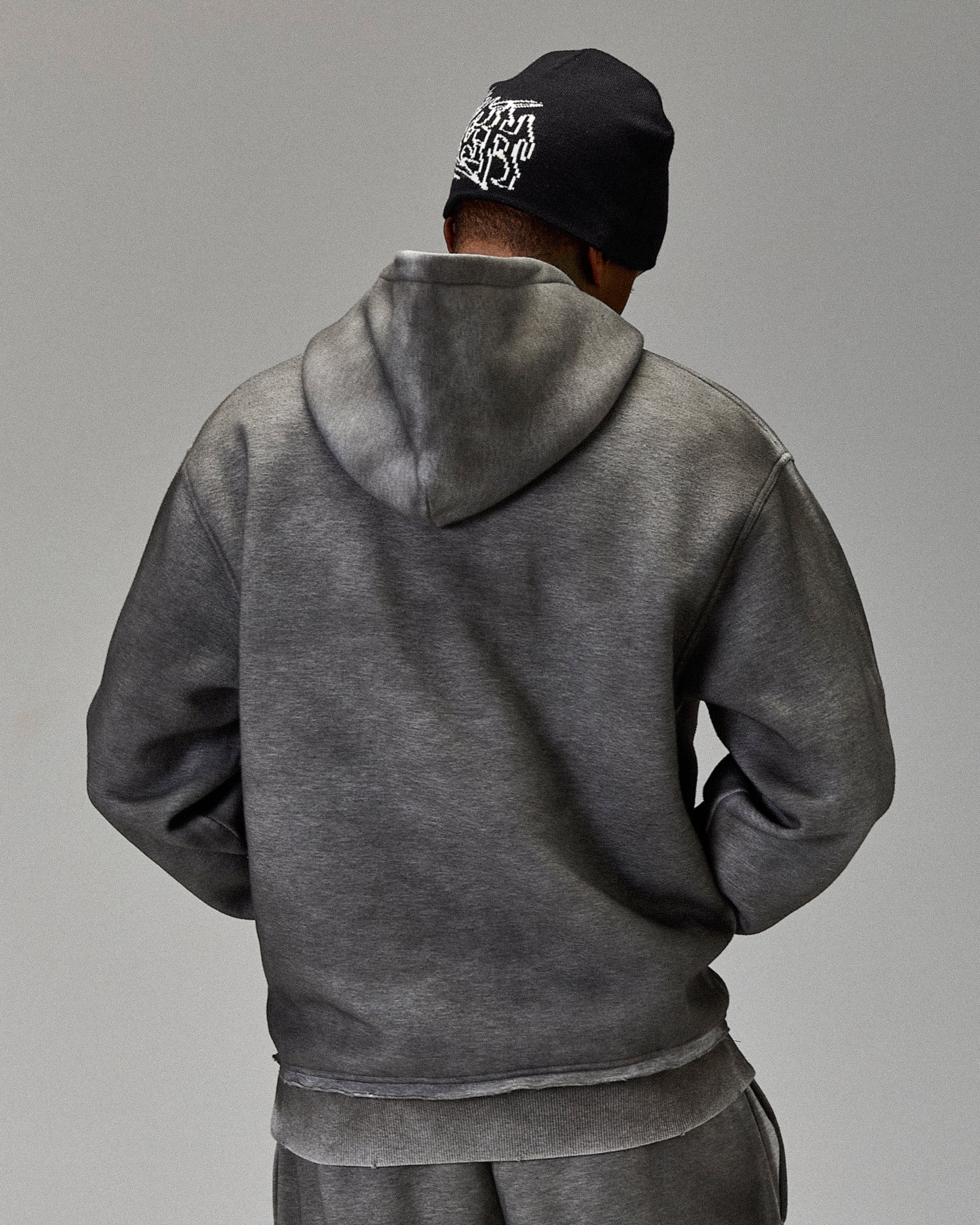 Person wearing a gray hoodie and black beanie with white logo on a gray background