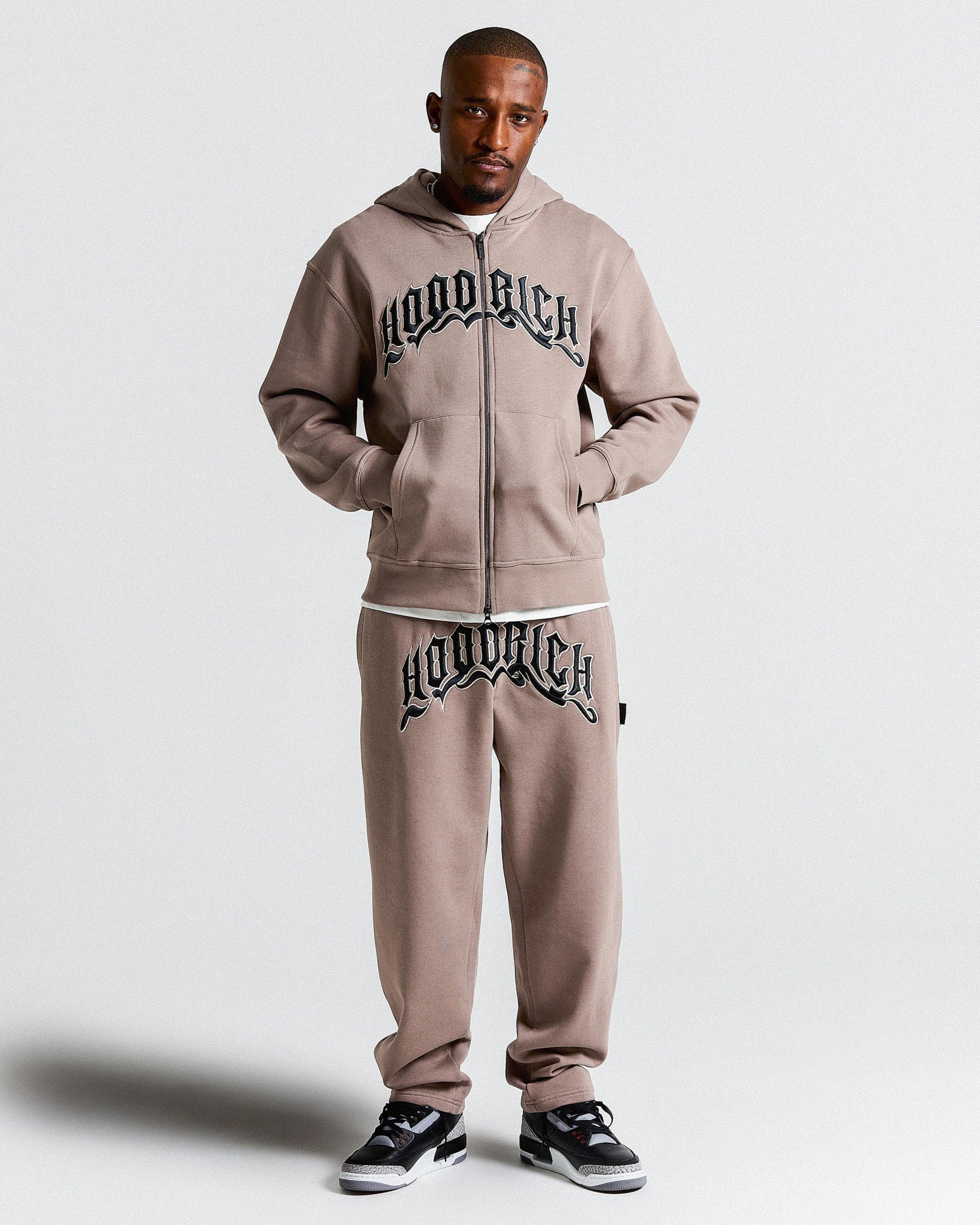 Man wearing a brown 'Hoodrich' tracksuit on a white background.