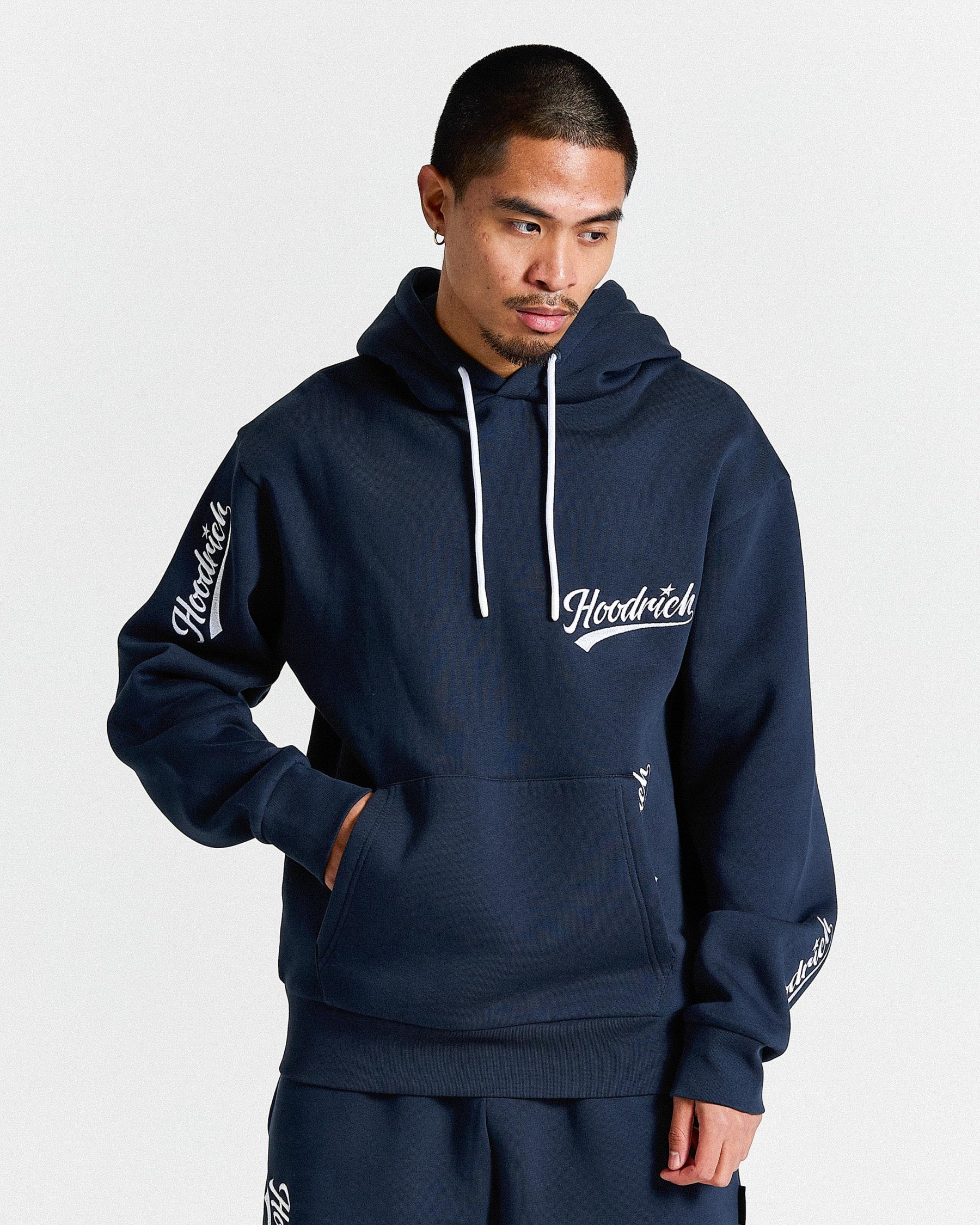 Man wearing a navy blue hoodie with 'Hoodrich' branding on a light gray background