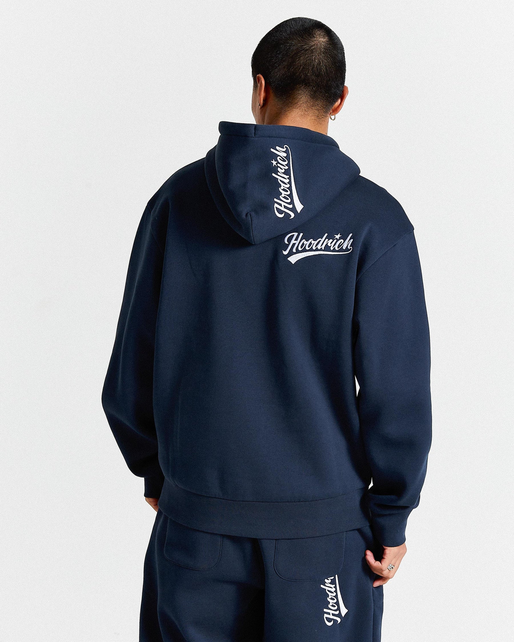 Person wearing a navy blue hoodie with 'Hoodrich' branding on the back against a light gray background