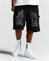 Person wearing black shorts with white text and white sneakers on a light gray background