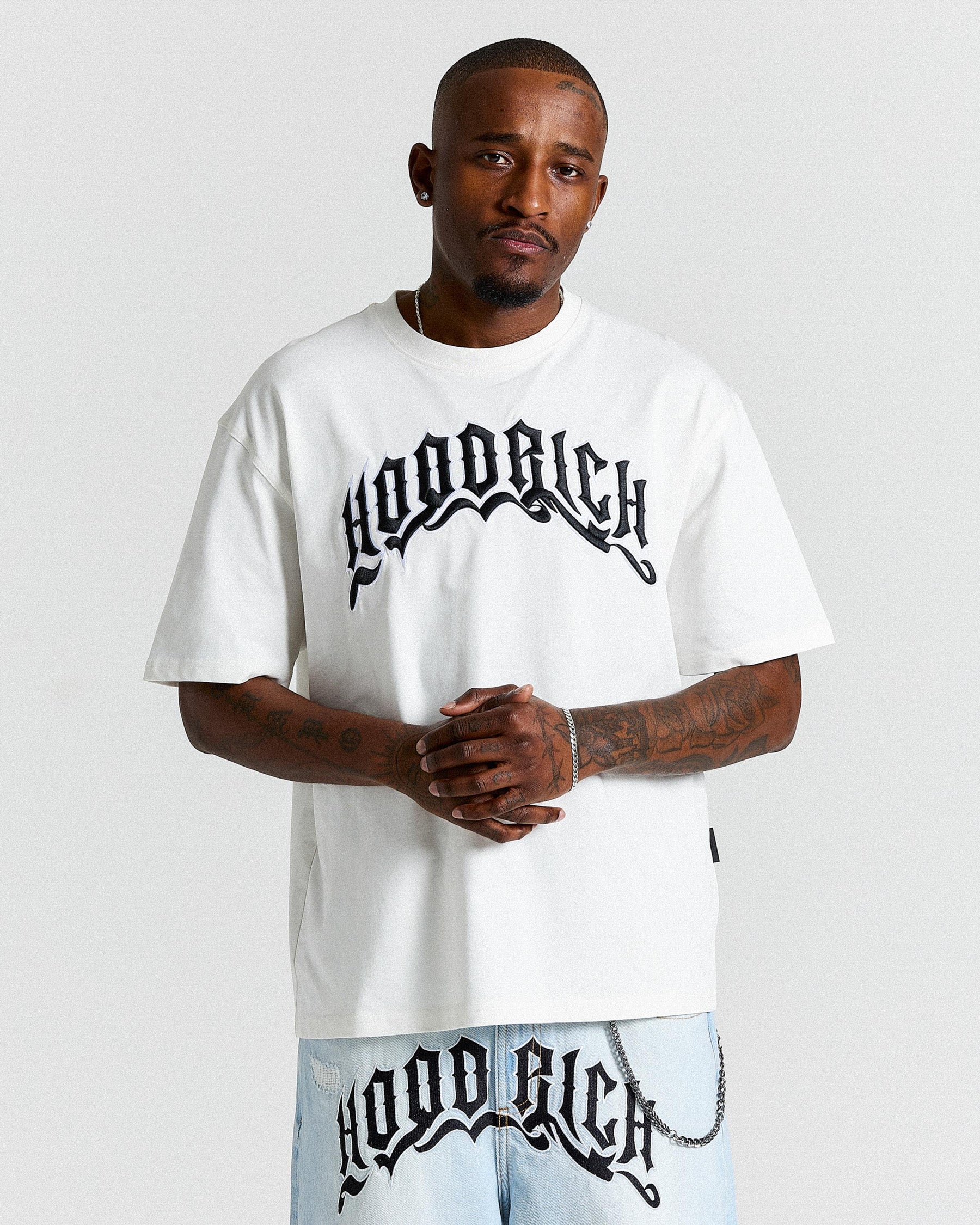 Man wearing a white 'Hoodrich' t-shirt and pants on a light gray background