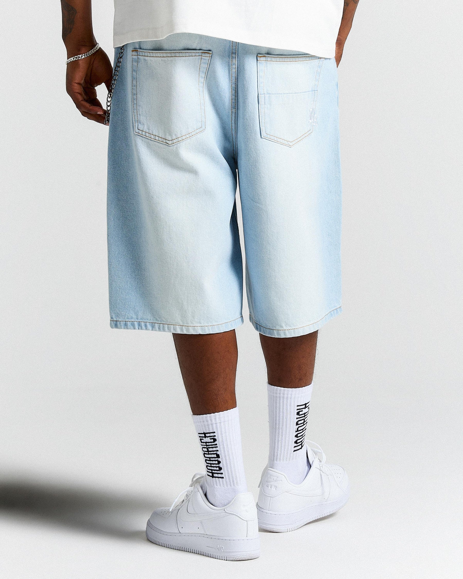 Person wearing light blue denim shorts and white sneakers on a plain background