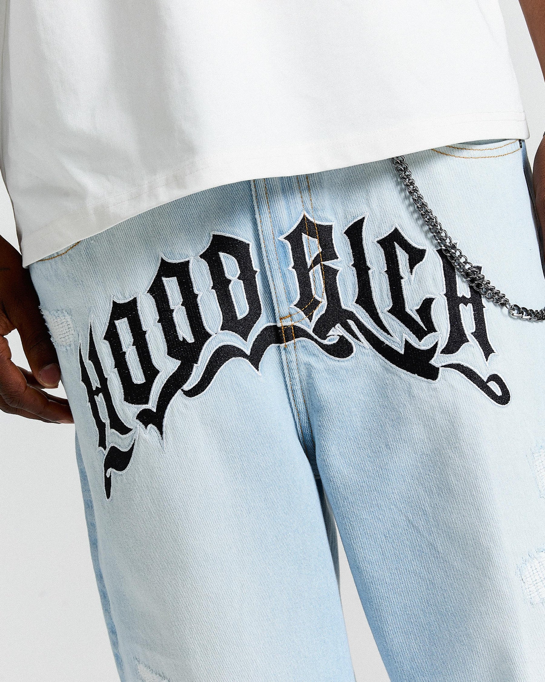 Light blue jeans with 'Hoodrich' text design worn by a person.