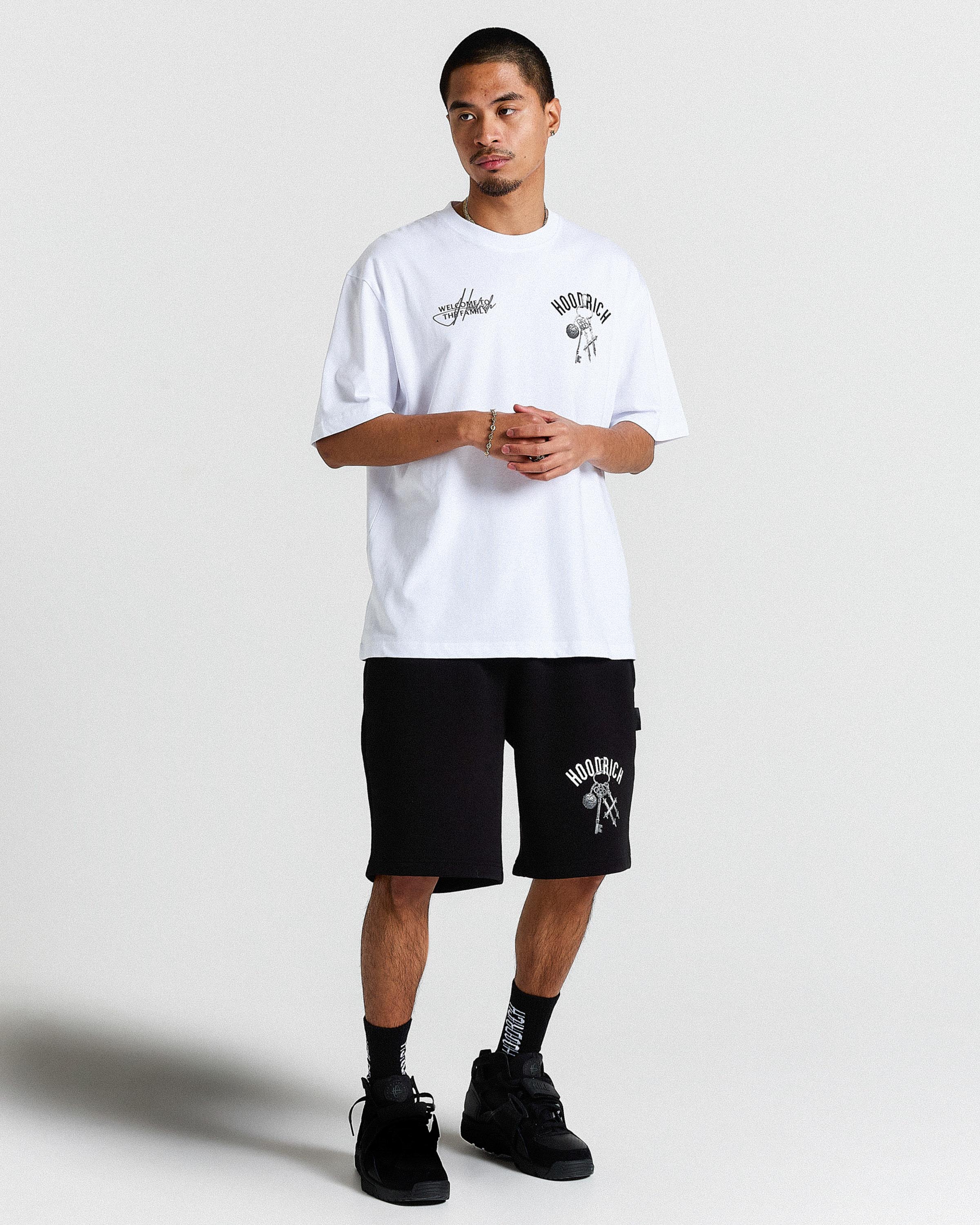 Person wearing a white t-shirt and black shorts with branding on a plain background
