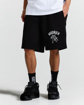 Person wearing black shorts with a logo and text, standing against a white background