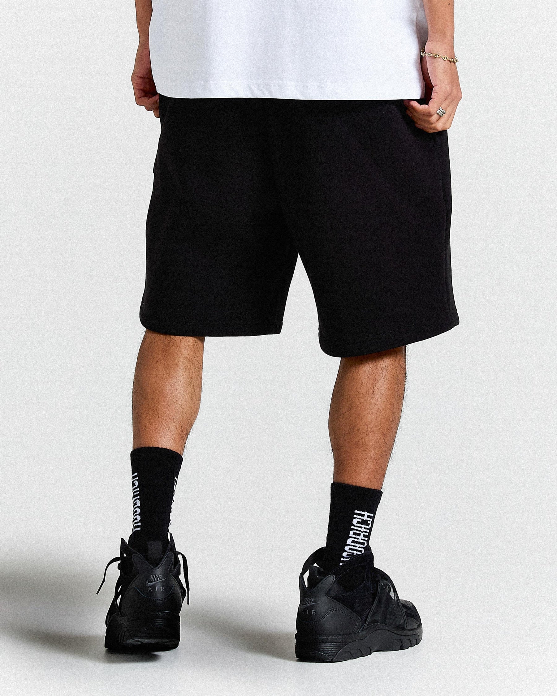Person wearing black shorts, white shirt, black shoes, and socks on a light gray background