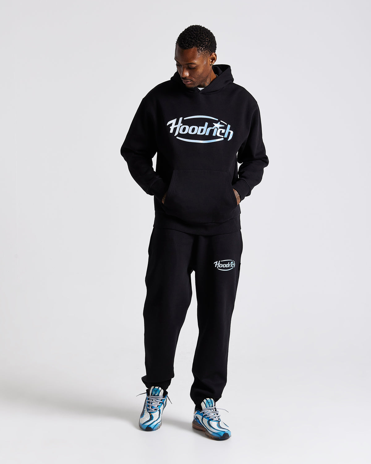 Displays a model wearing the Black 'Hoodrich' branded men's Curve Full Tracksuit 