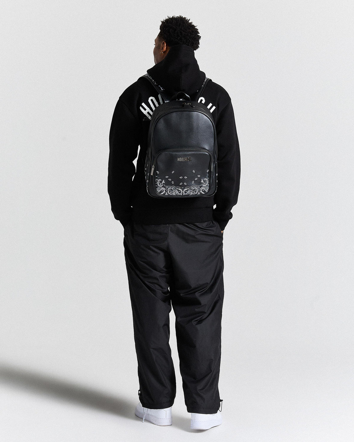 Person wearing a black tracksuit with a backpack on a white background