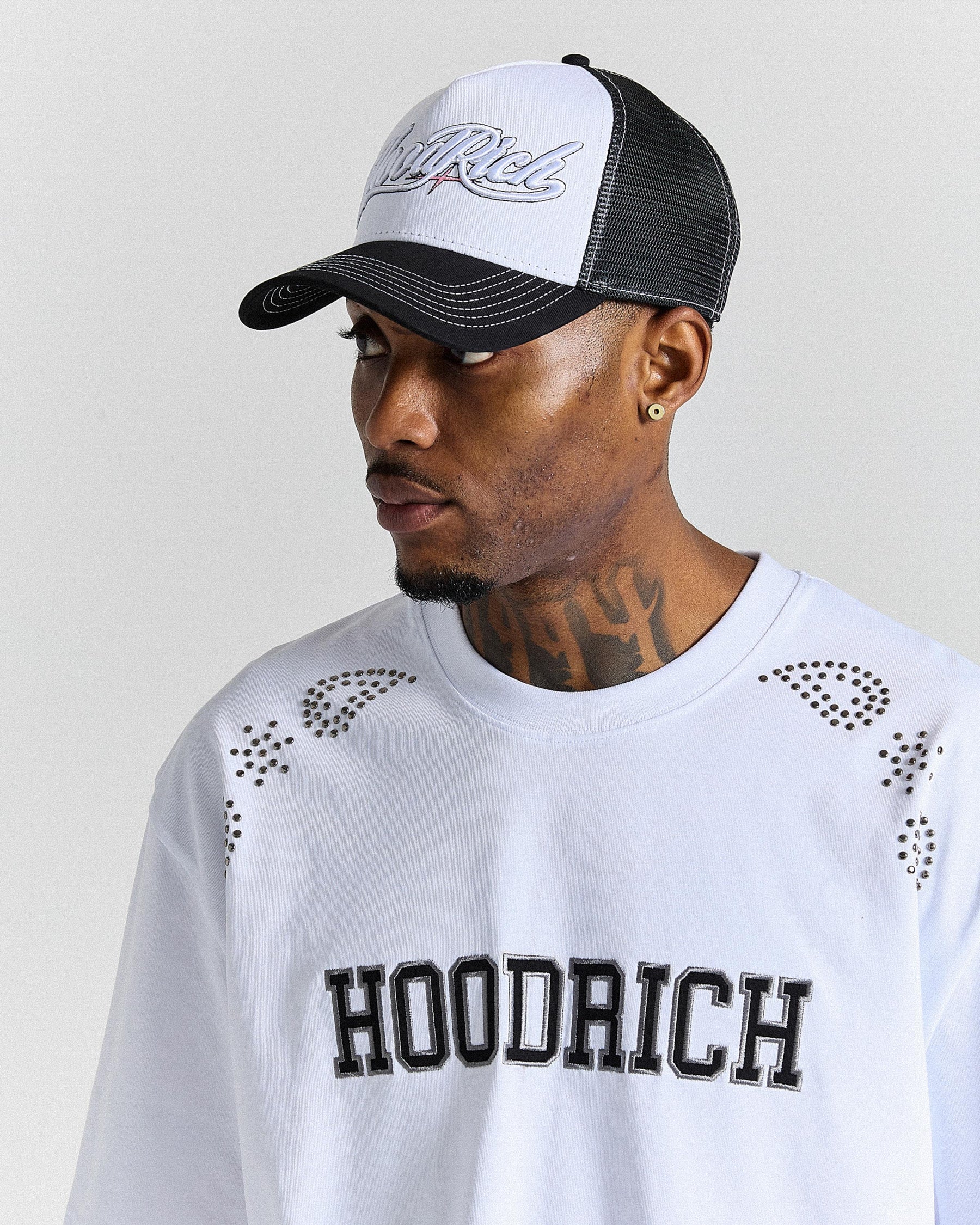 Man wearing a white cap with black brim and 'Hoodrich' logo, and a white shirt with 'Hoodrich' text.