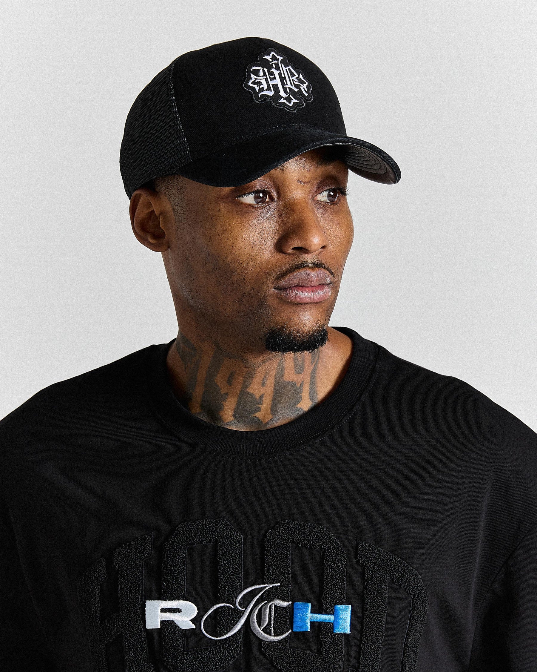 Man wearing a black cap and black shirt with 'HOODRICH' logo on a light gray background