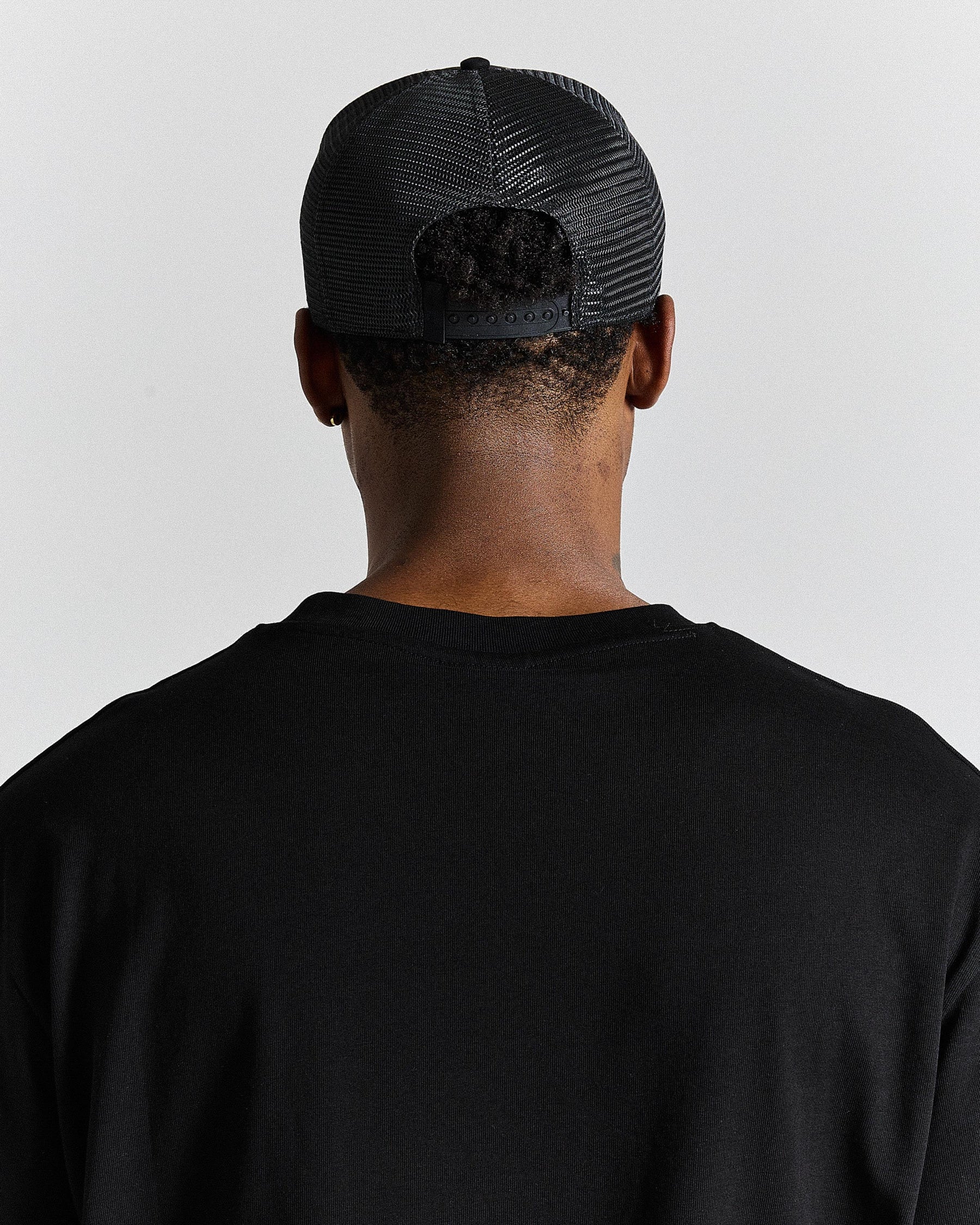 Person wearing a black cap and black shirt against a light gray background