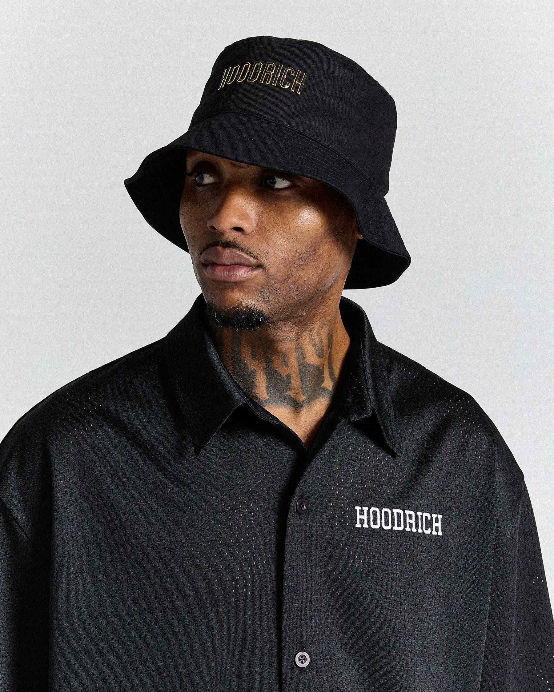 Man wearing a black 'Hoodrich' bucket hat and shirt against a gray background