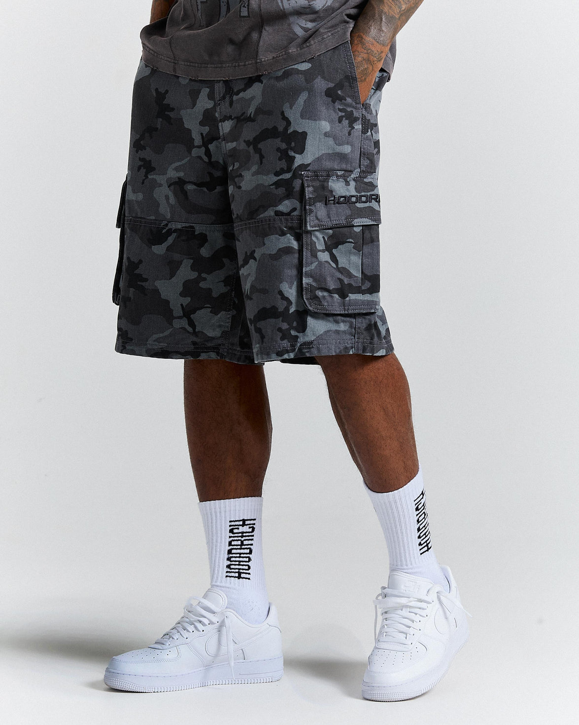 Person wearing camouflage shorts and white sneakers with visible branding on a plain background
