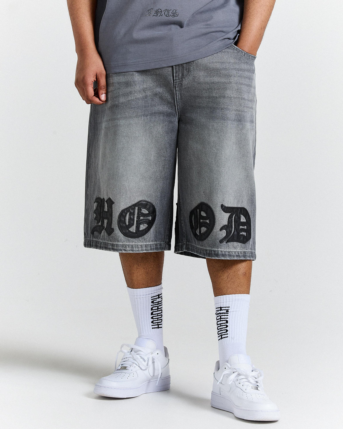 Person wearing gray denim shorts with black designs and white sneakers on a white background