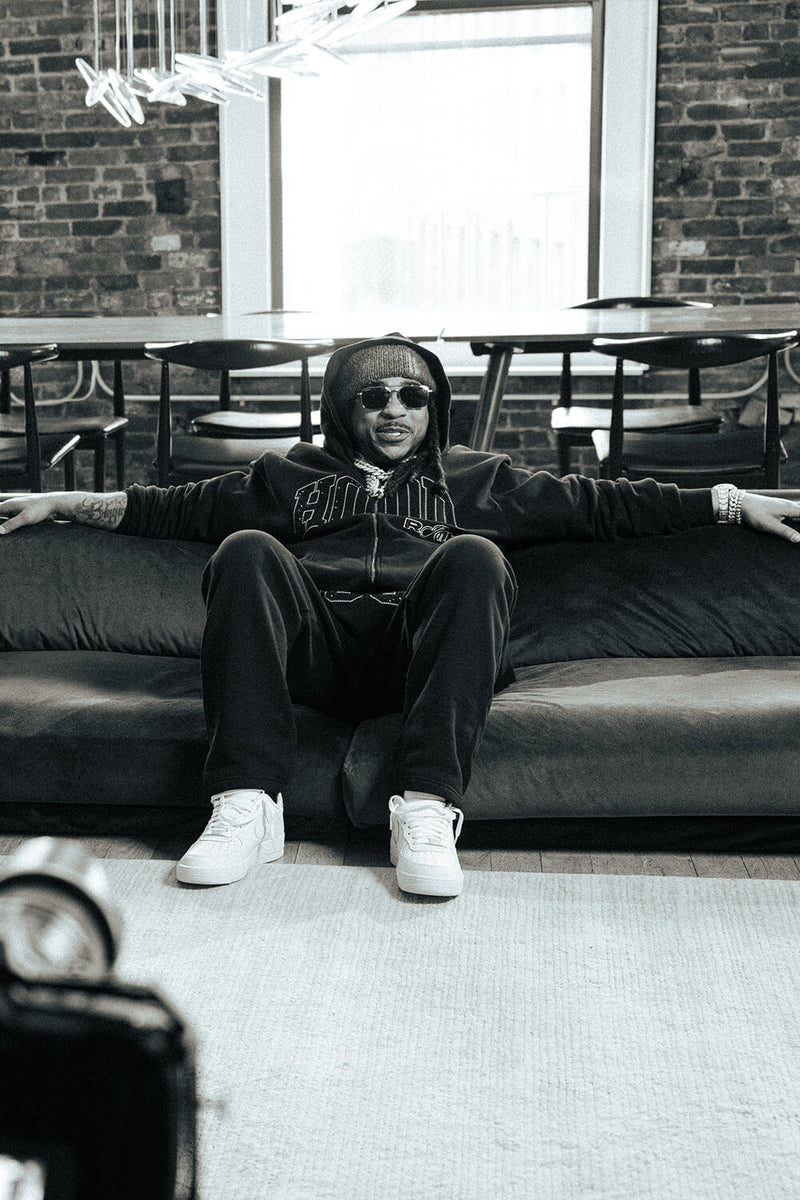 Person sitting on a couch in a modern indoor setting with large windows and brick walls.